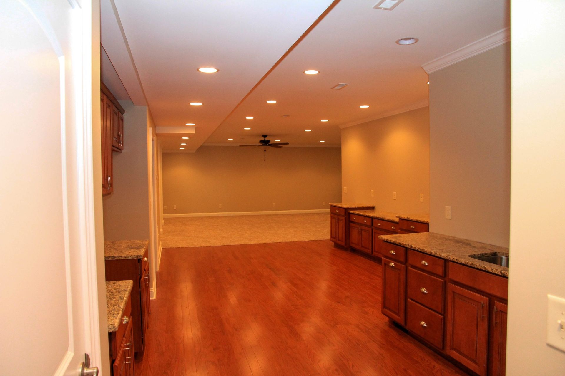 Empty basement room with wood floors, recessed lights, and built-in cabinets along the right wall