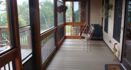 Covered porch with wooden railing, hanging plants, and two chairs overlooking trees