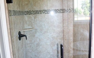 Glass shower enclosure with beige tiled walls and a wall-mounted black shower handle