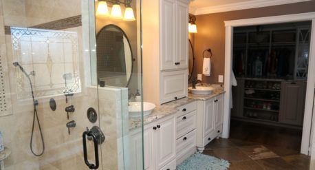Bathroom with glass shower, vanity sink, white cabinets, and open doorway to a dark walk-in closet.