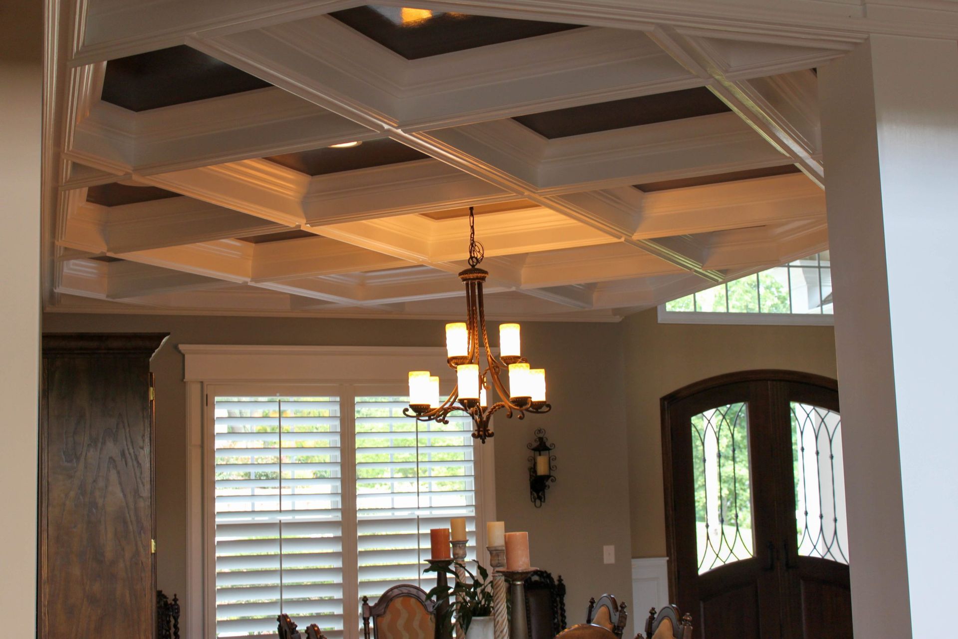 Dining room with a tray ceiling, chandelier, windows with shutters, and a front door with glass panes