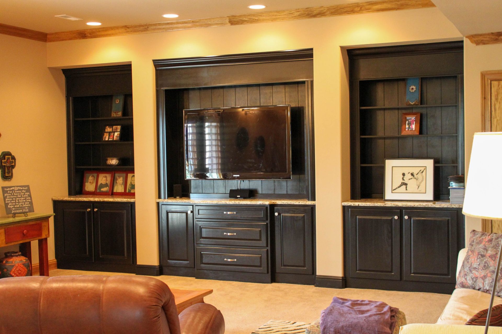 Living room with dark wood built-in cabinets, a TV, and a leather sofa under warm lighting