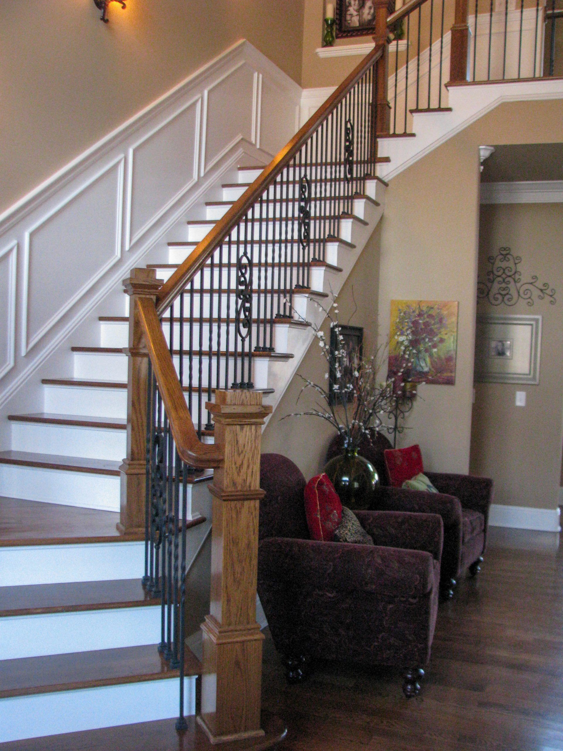 Indoor staircase with dark wood banister, two upholstered chairs, and a lamp in a foyer.