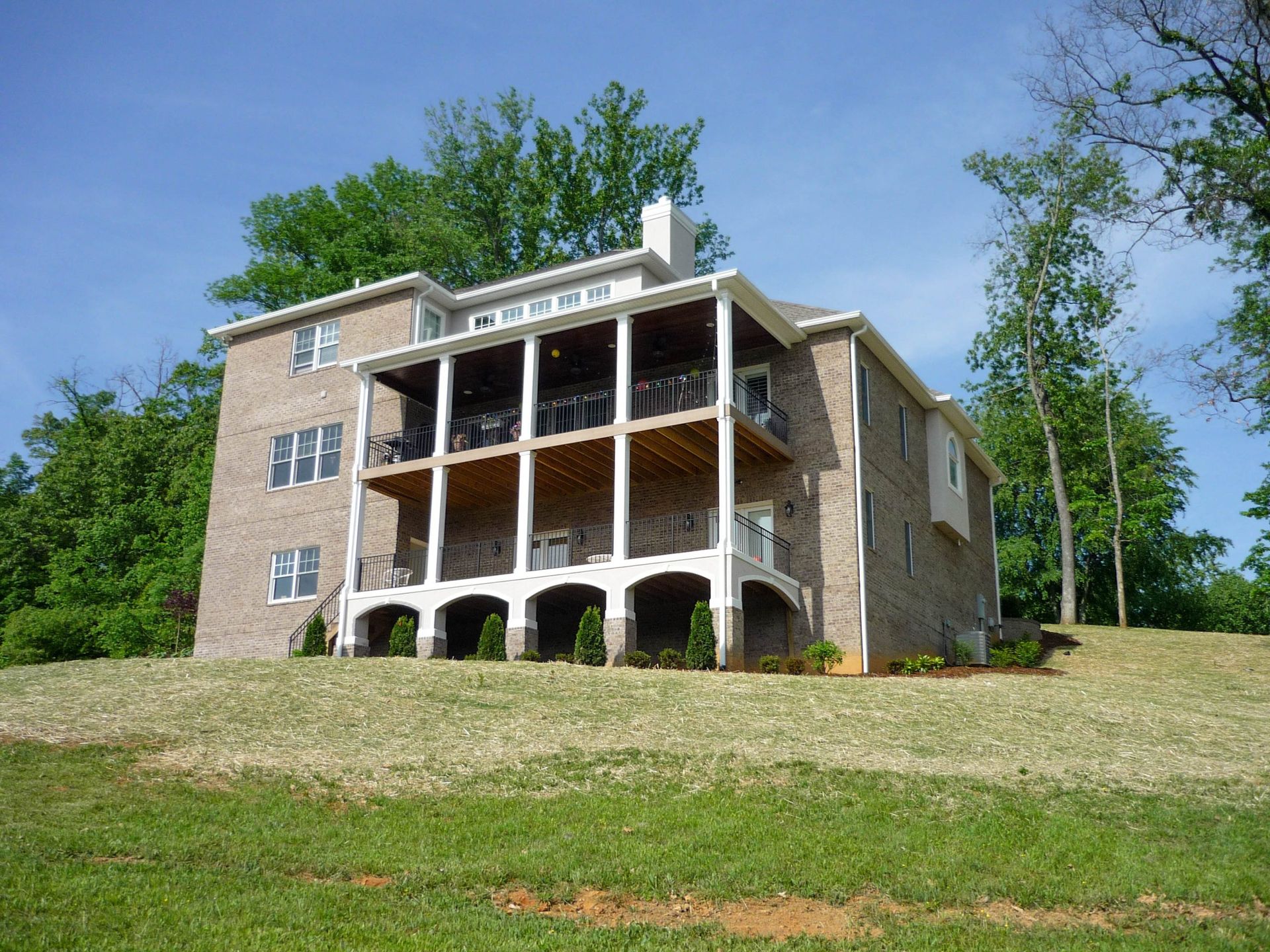 Stone house with white porch columns on a grassy hill under a blue sky
