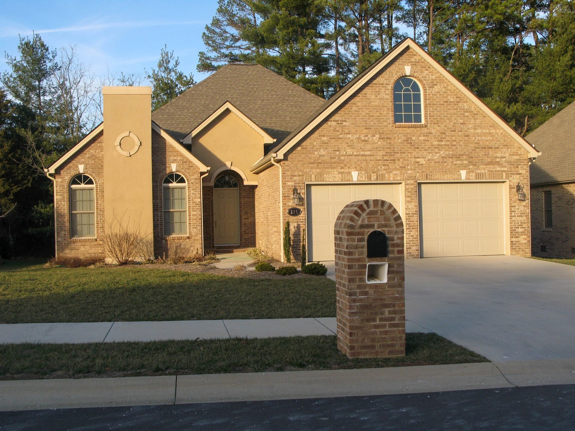 Brick suburban house with arched entry, two garages, and a mailbox in front