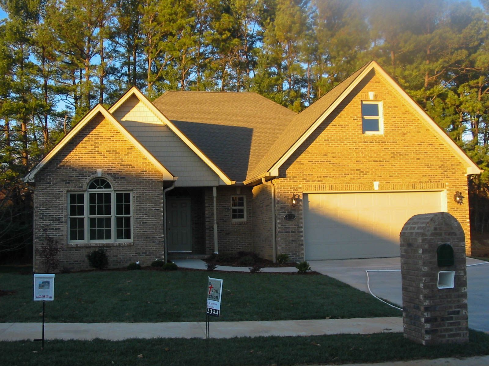 Suburban house with stone and yellow siding, front lawn, driveway, and brick mailbox at sunset
