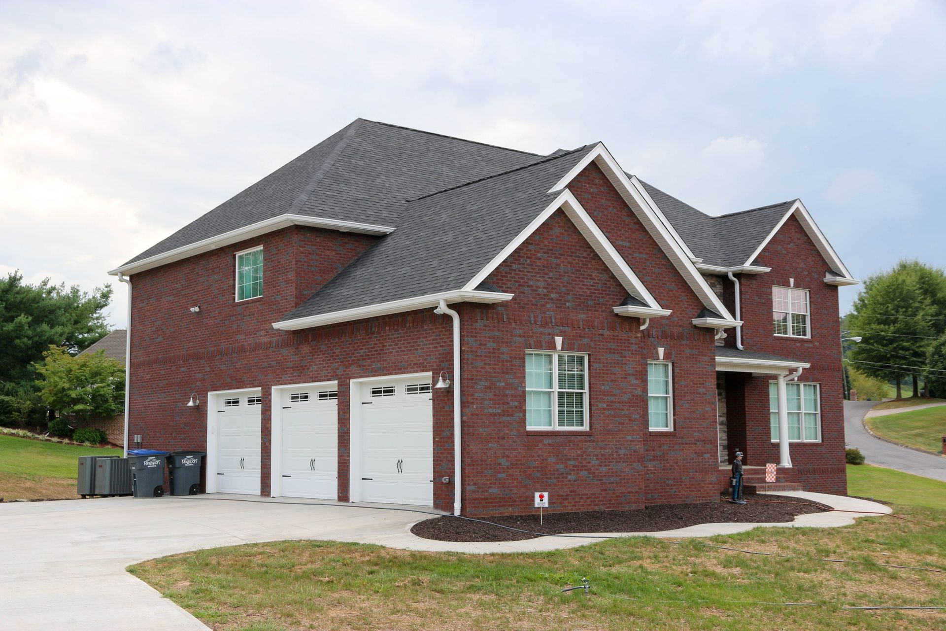 Brick two-story suburban house with three white garage doors and a front porch