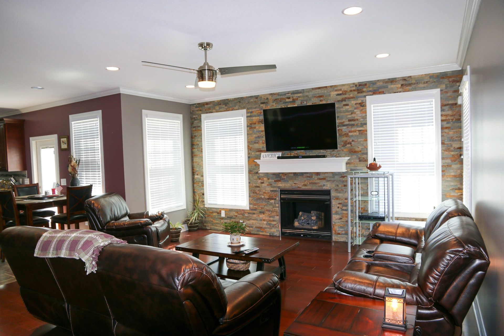 Modern living room with leather sofas, stone fireplace, wall-mounted TV, and large windows
