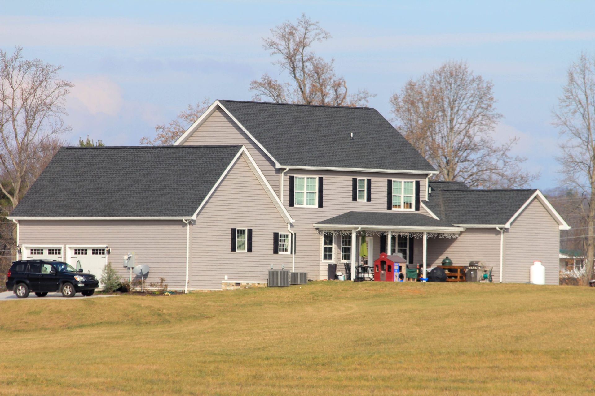 Large beige suburban house with a gray roof and front porch on a grassy lot under a blue sky