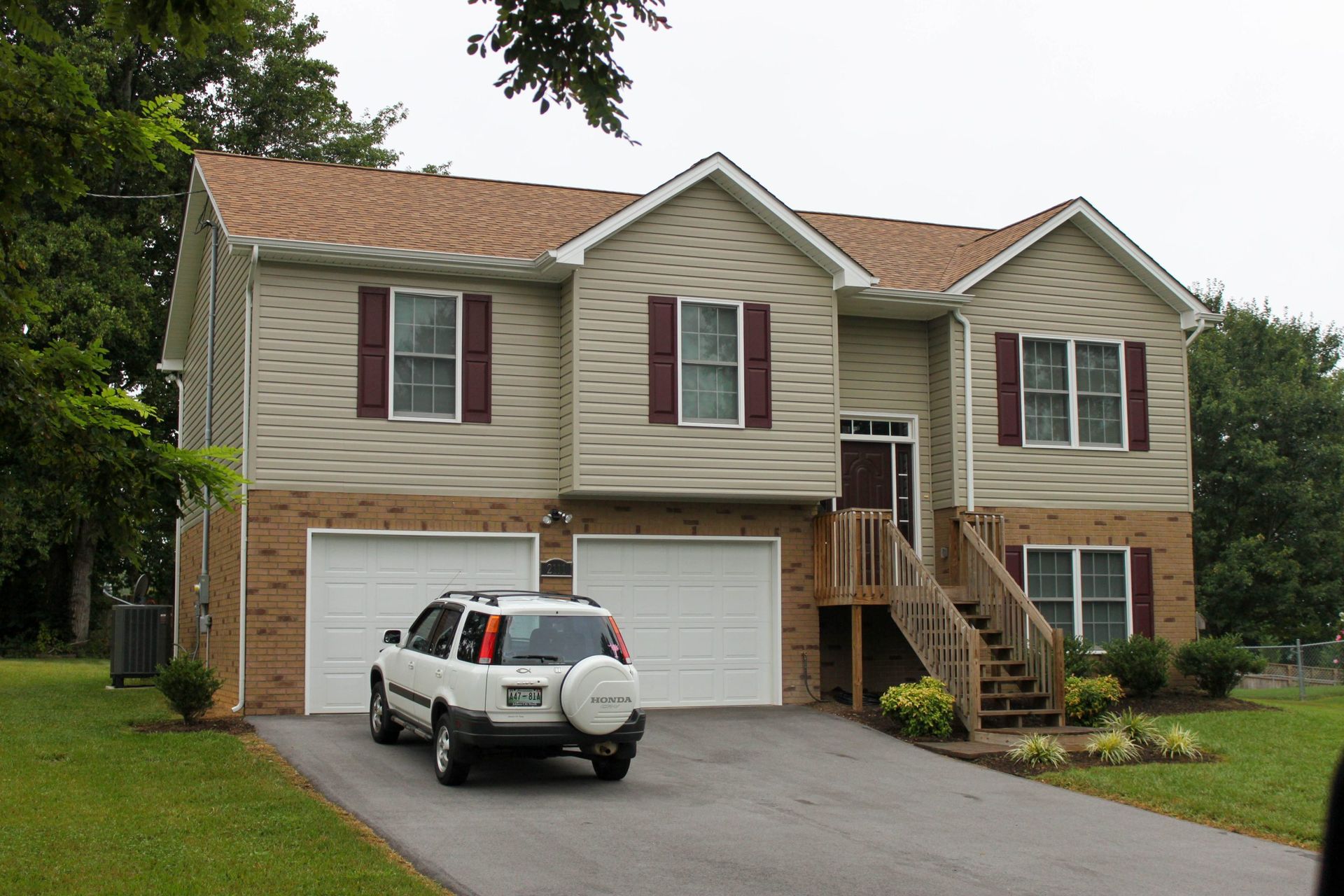 Suburban house with two garages, a white SUV in the driveway, and an exterior stairway to the front door