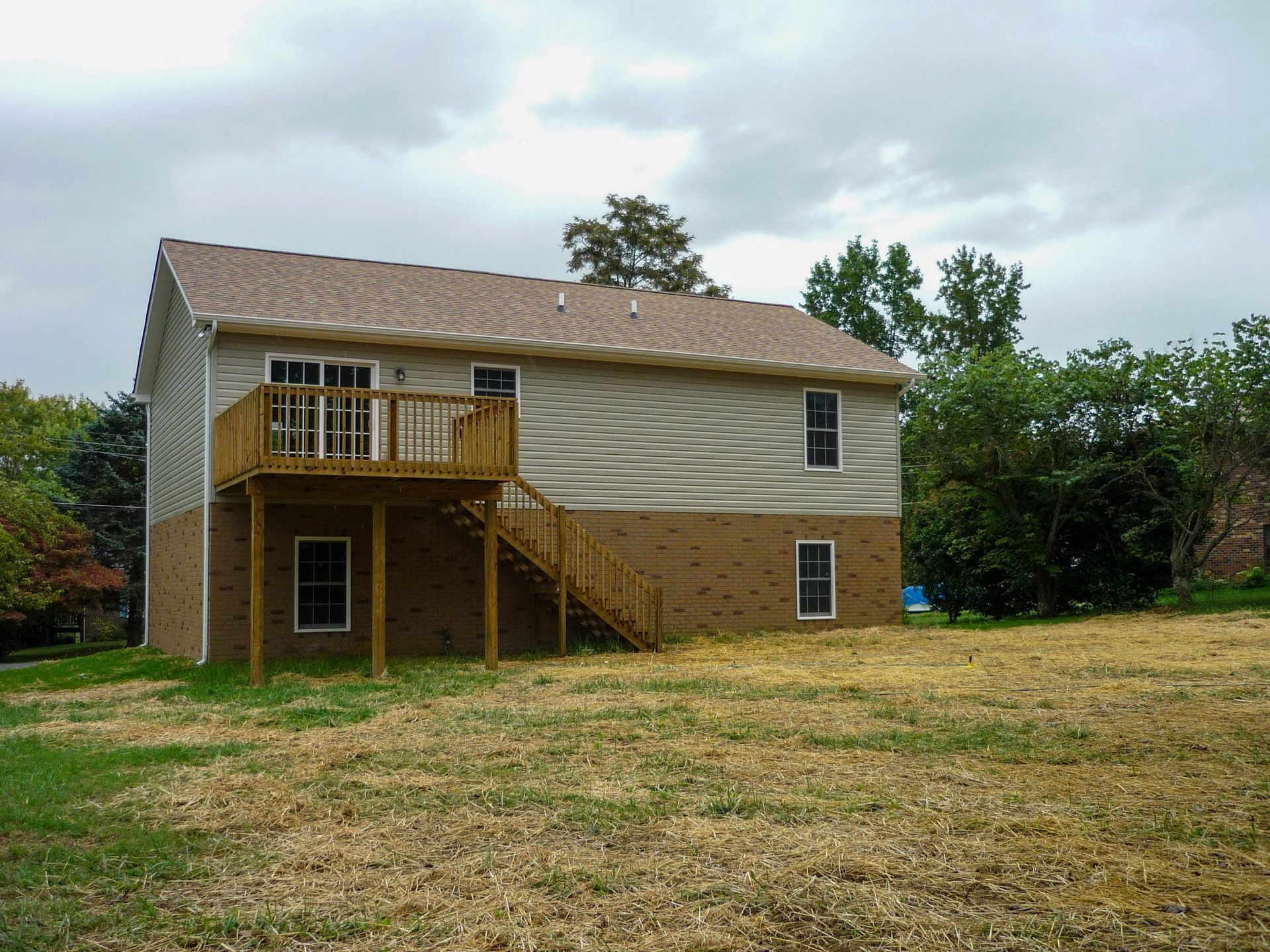 Two-story tan house with a deck and stairs, on a grassy yard under a cloudy sky