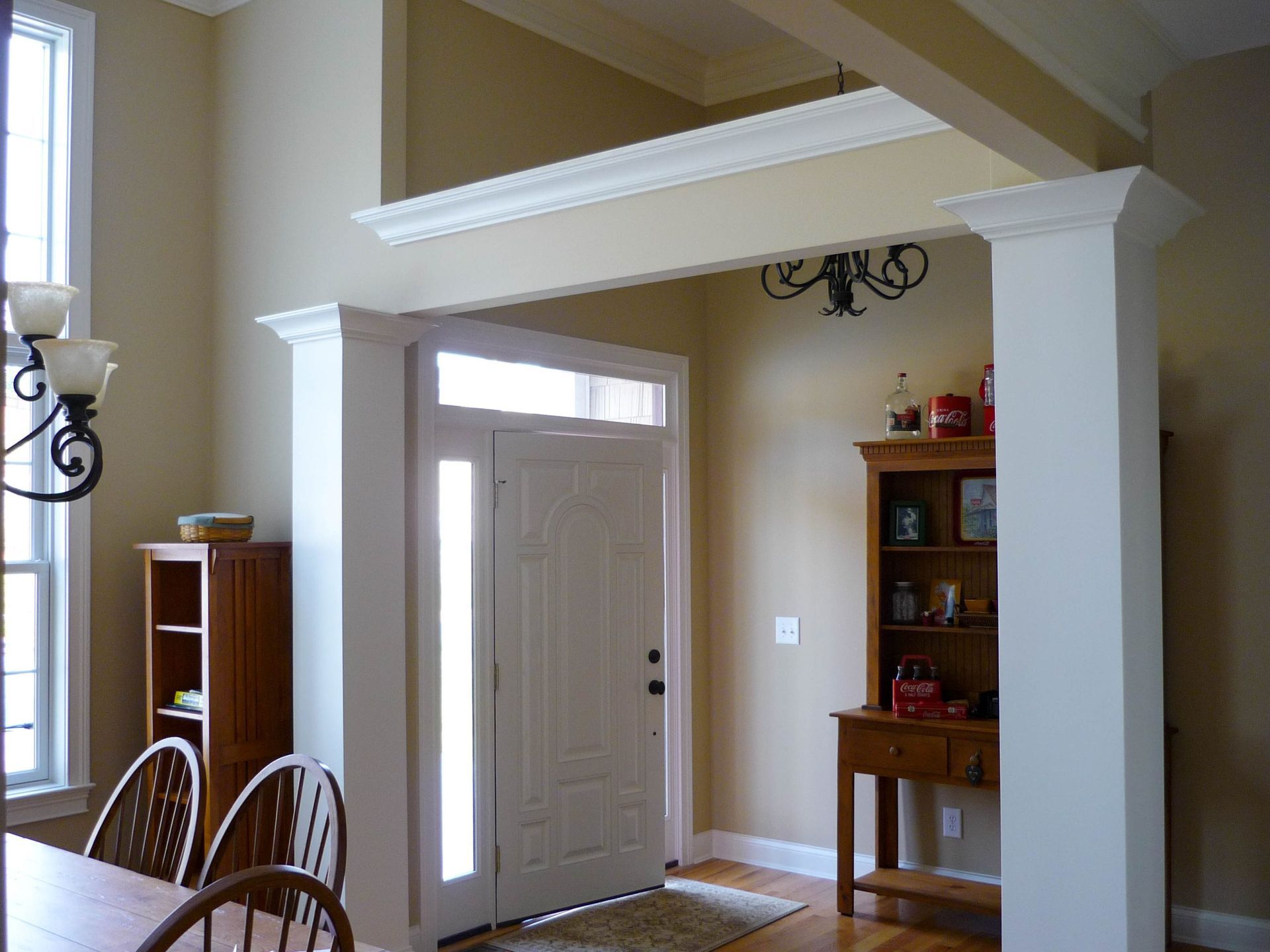 Bright foyer with white entry columns, front door, and a wooden display cabinet