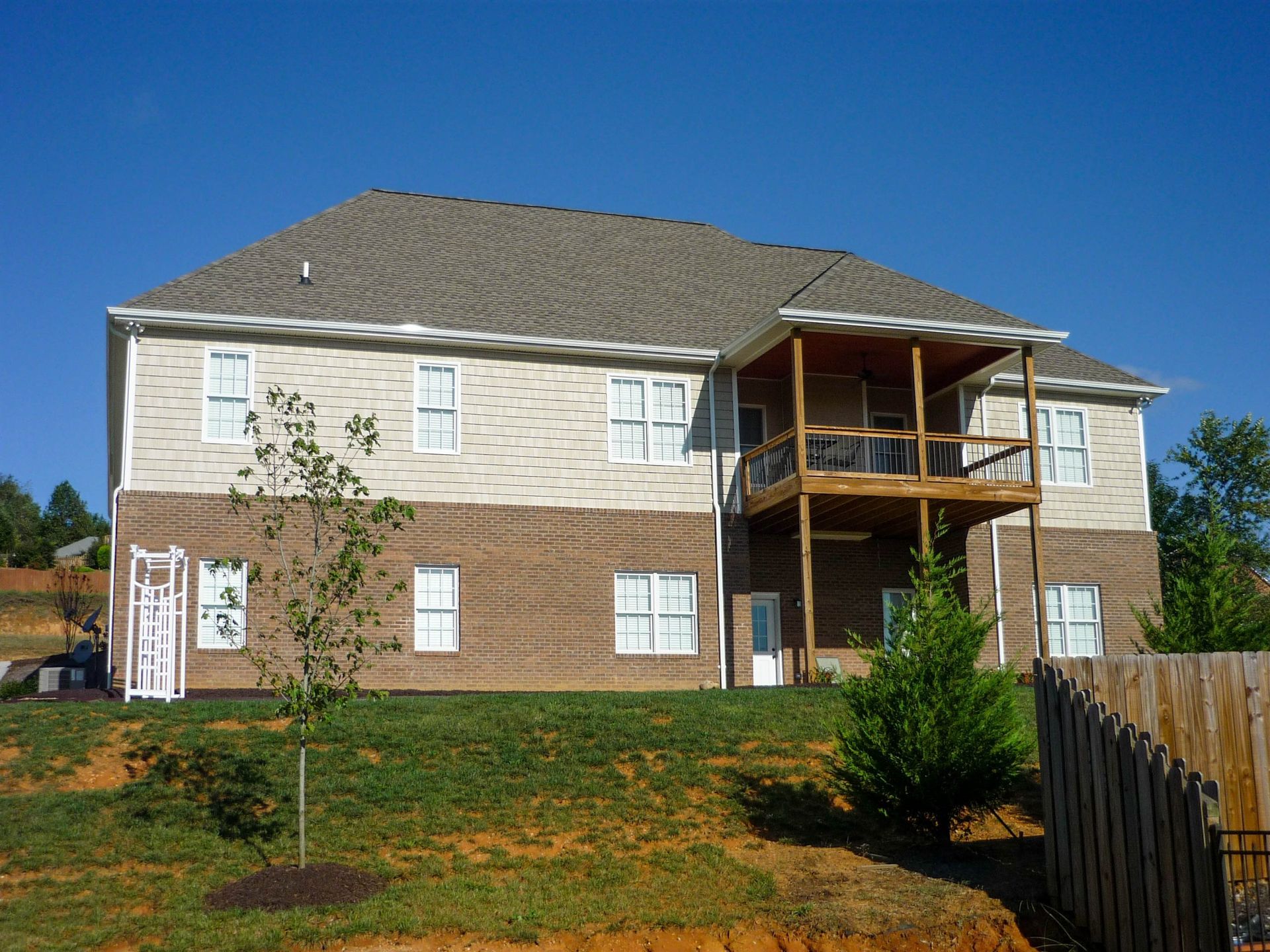 Two-story beige house with white-trim windows and a wooden balcony under a blue sky