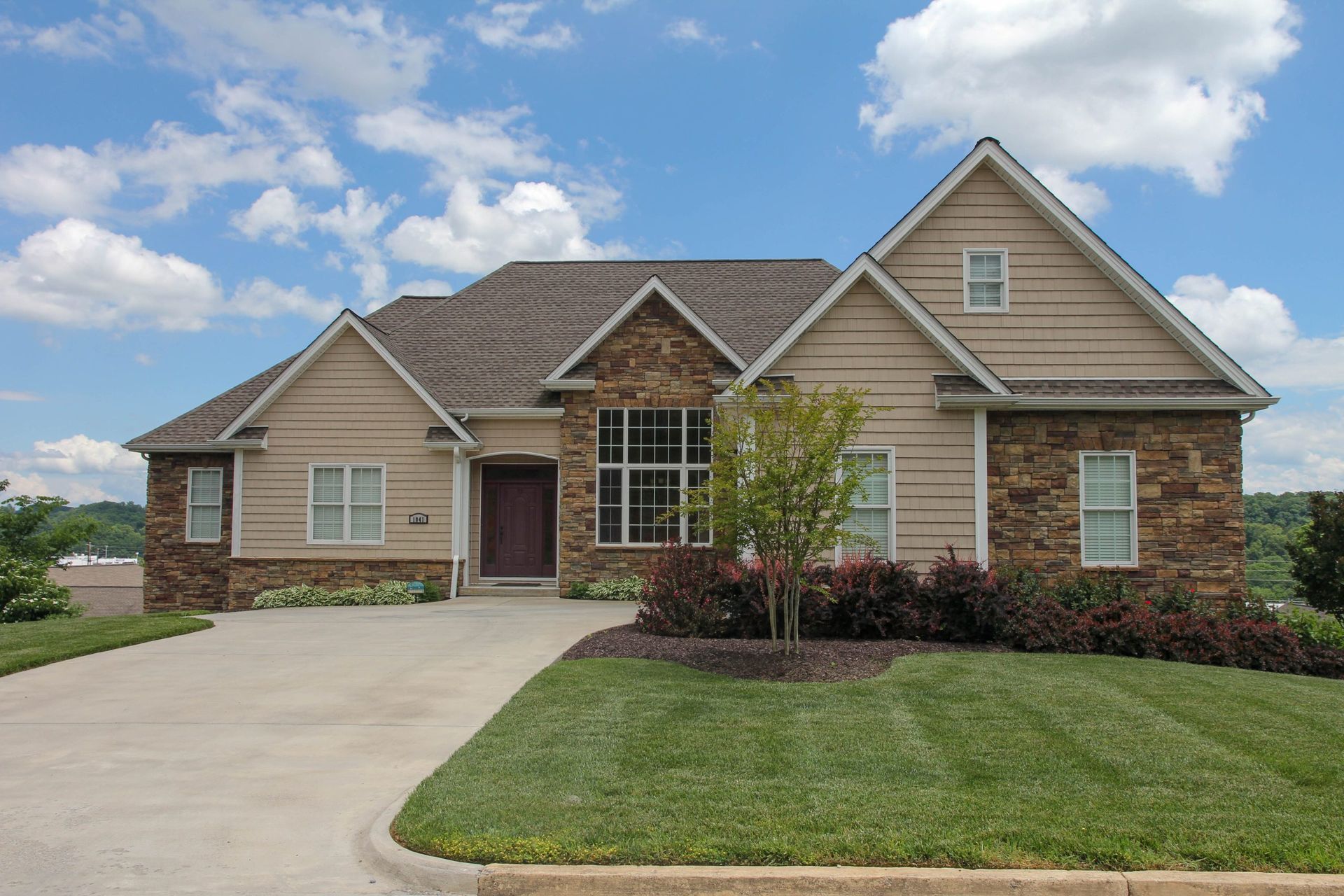 Suburban house with brick and tan siding, a driveway, and a neatly trimmed front lawn under a blue sky