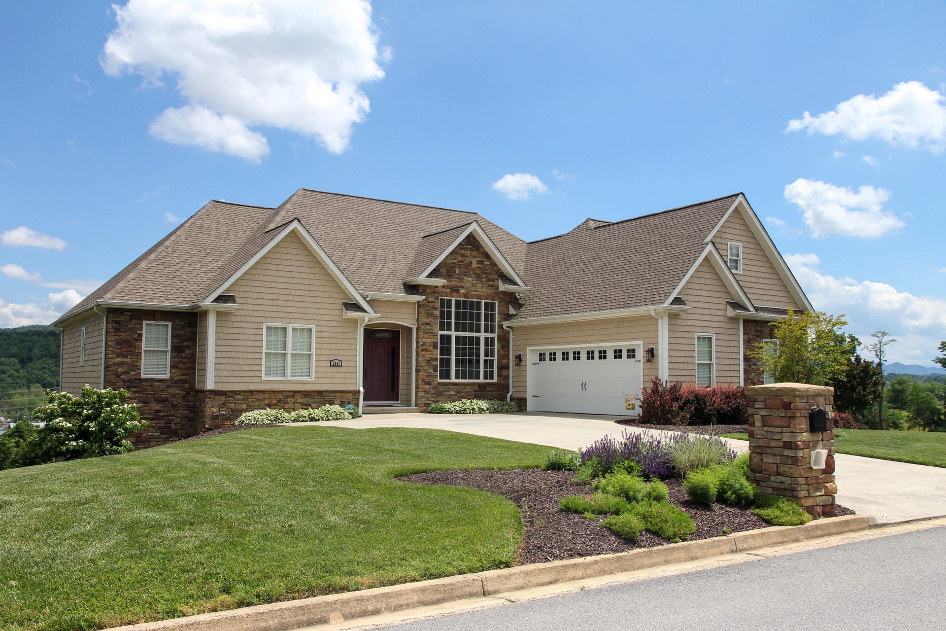 Suburban brick house with beige roof, front lawn, driveway, and blue sky on a sunny day