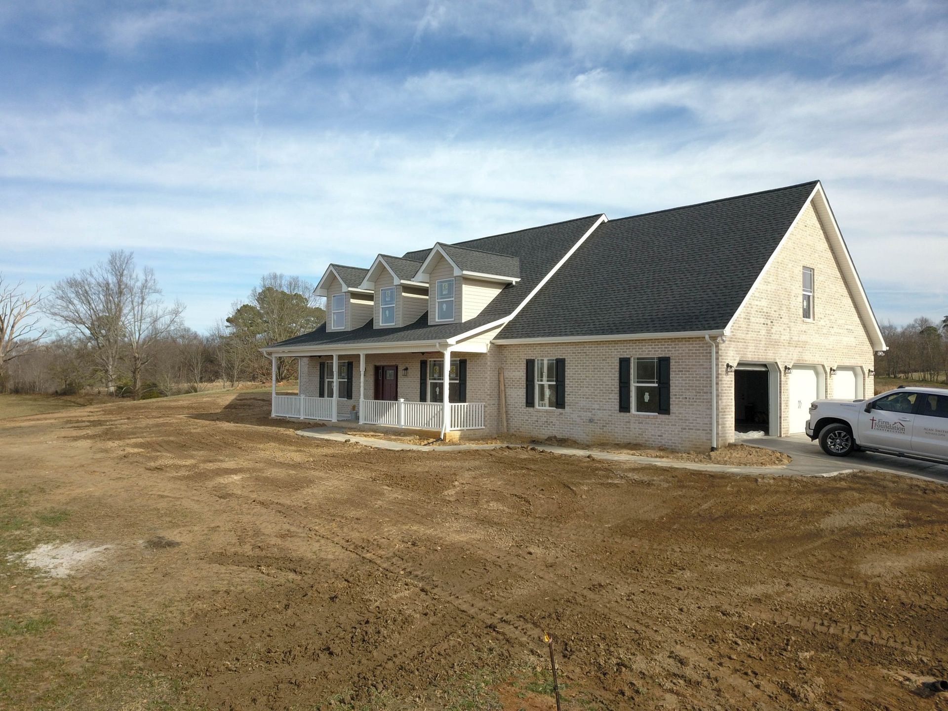 Rural house with beige siding and black roof on a grassy lot under a blue sky
