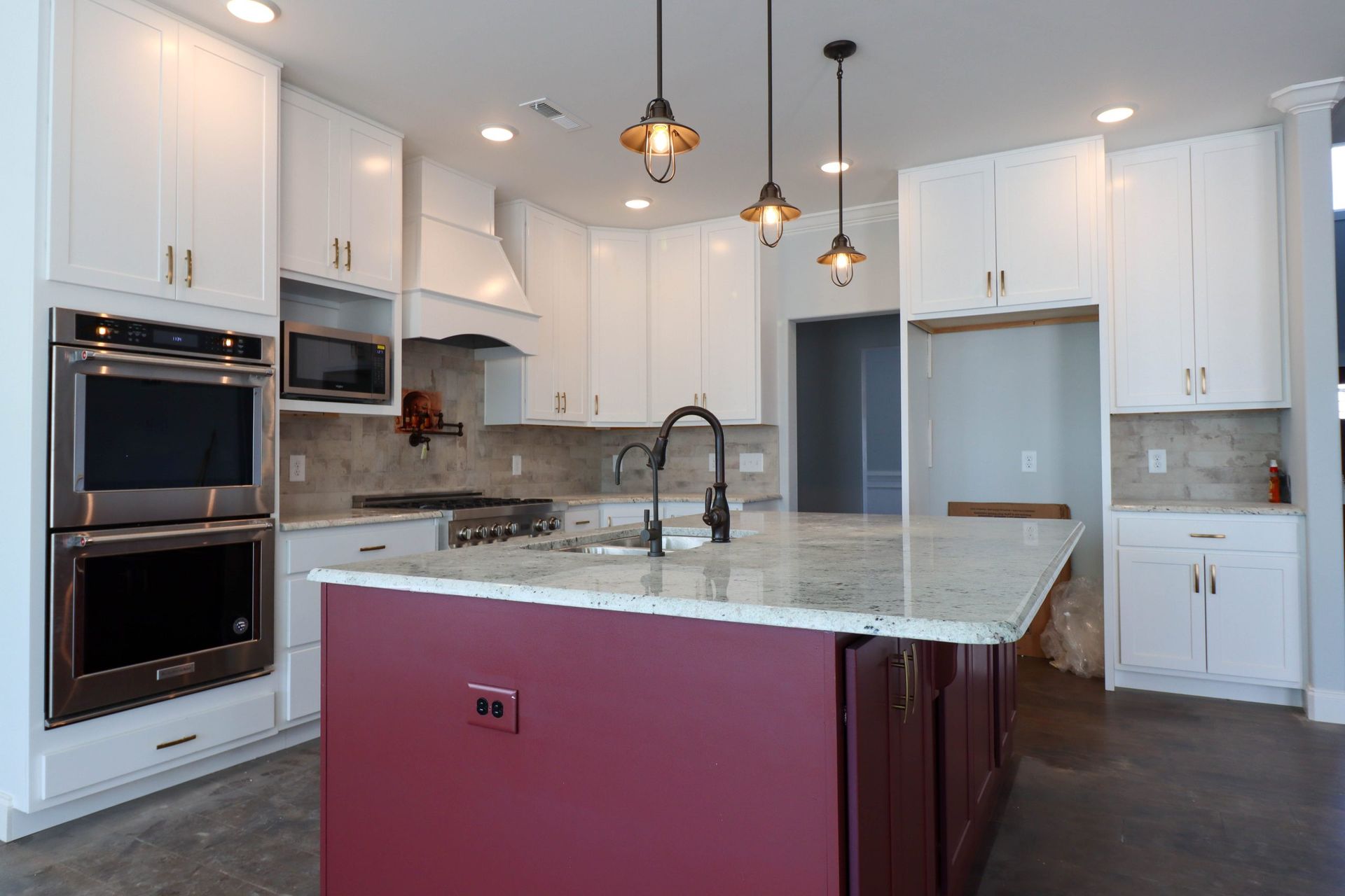 Modern white kitchen with marble island, black fixtures, pendant lights, and burgundy island base