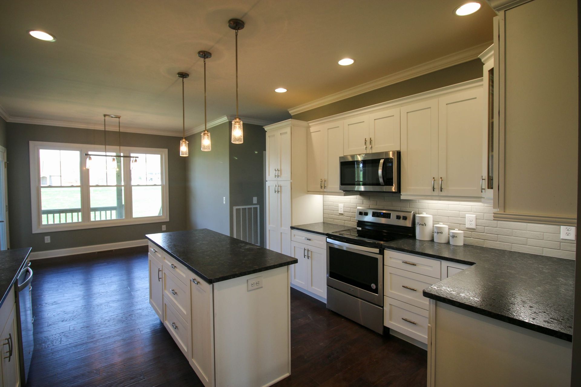 Bright modern kitchen with white cabinets, granite countertops, island, stainless steel appliances, and pendant lights