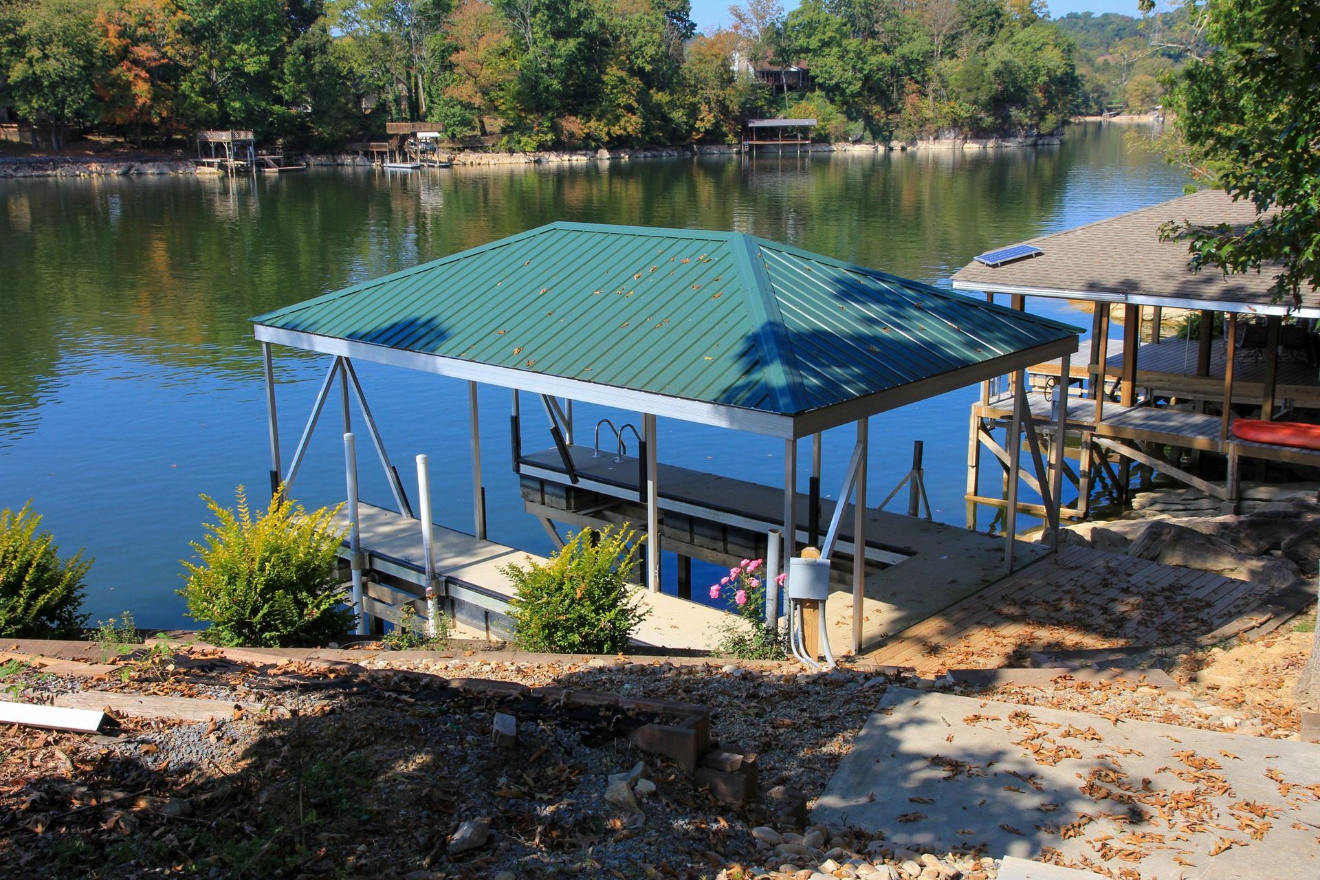 Small green-roofed dock pavilion by a calm lake with trees and a sandy shore