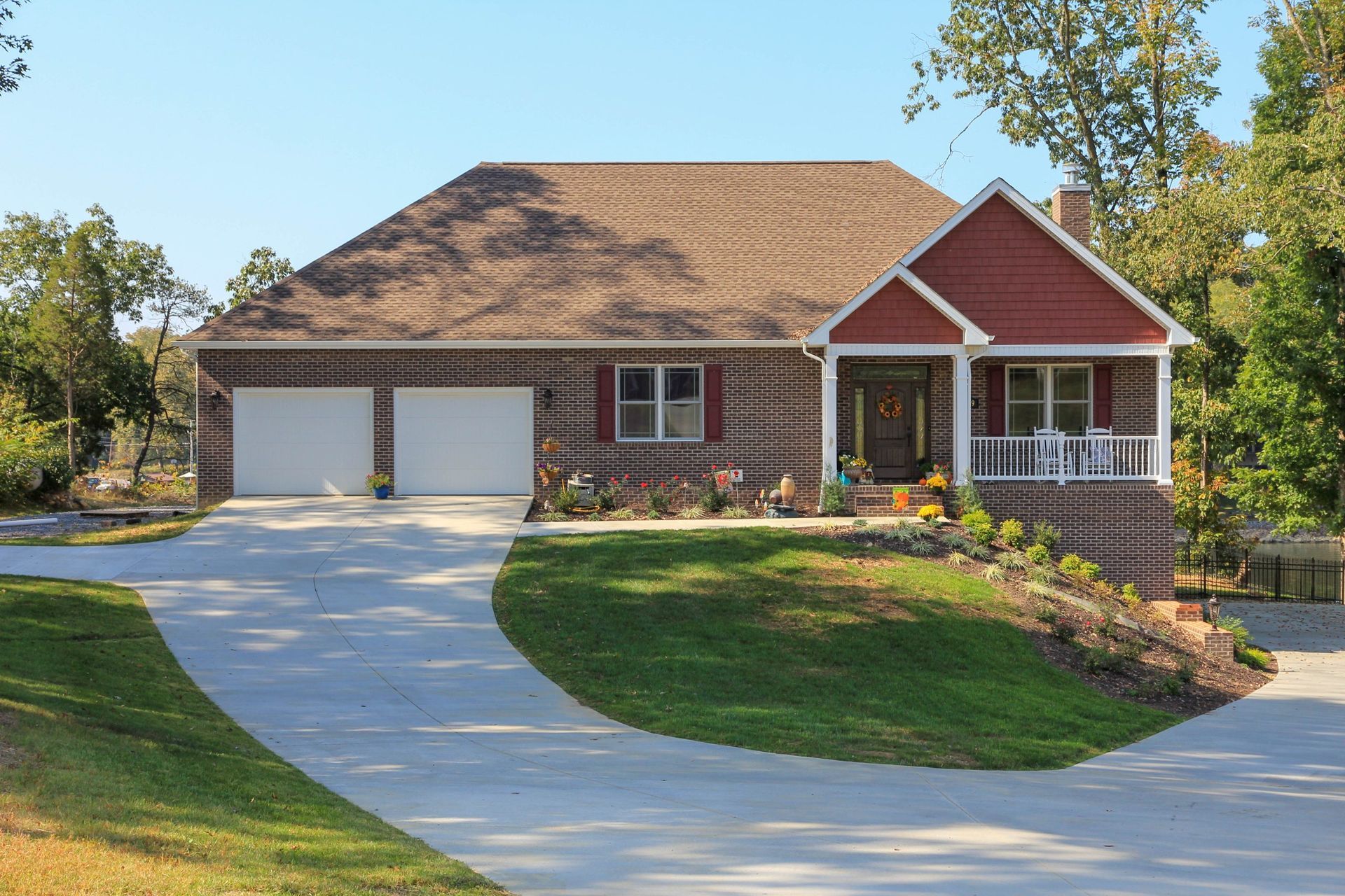 Suburban house with red siding, two-car garage, and a curved concrete driveway surrounded by green lawn.