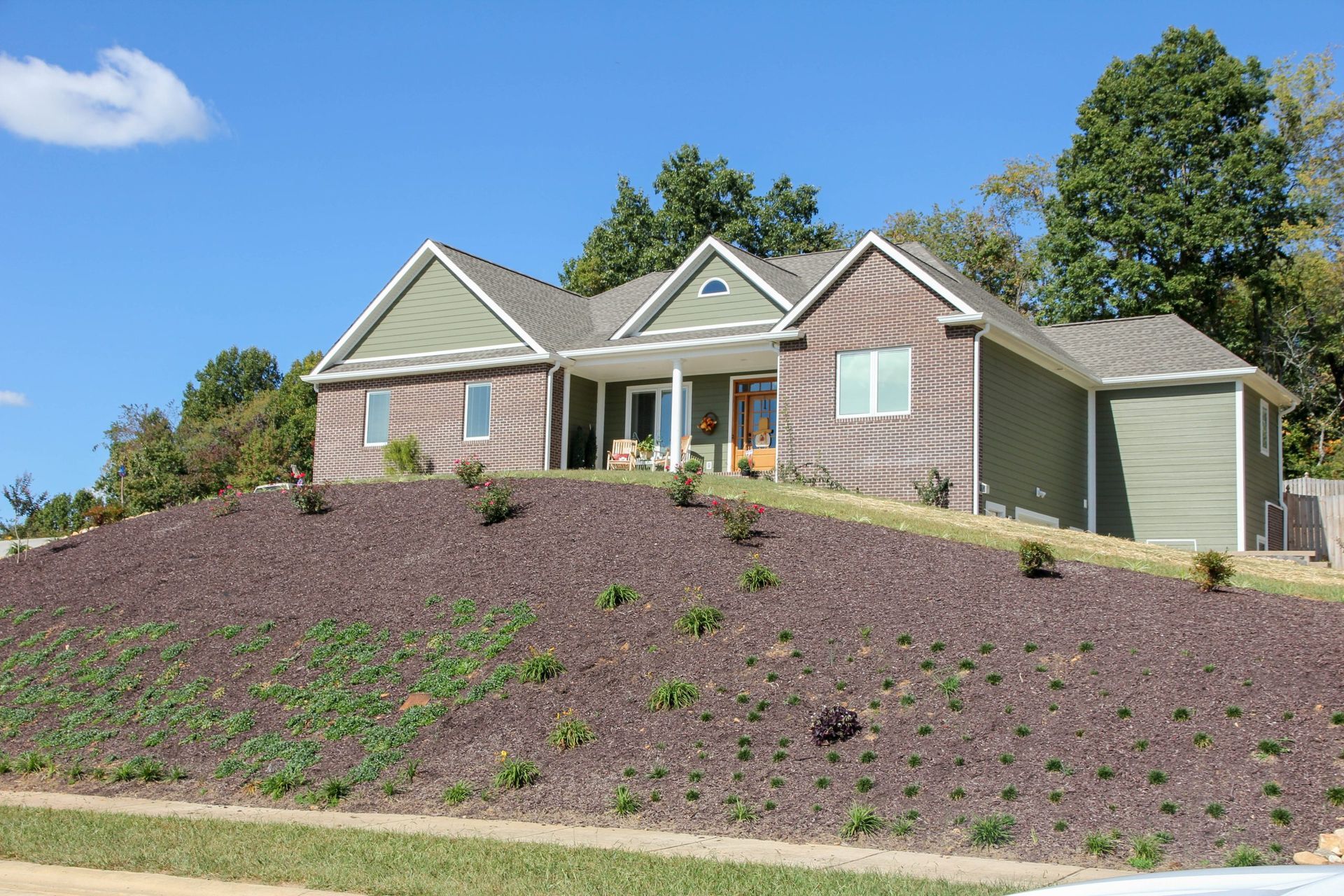 Single-story house with gray siding and a large mulched front slope under a blue sky.