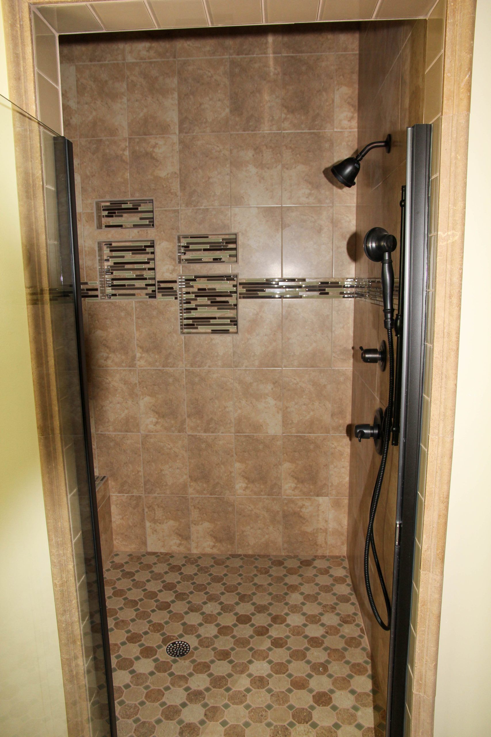 Small tiled shower with brown walls, decorative border tile, and black showerhead and controls.