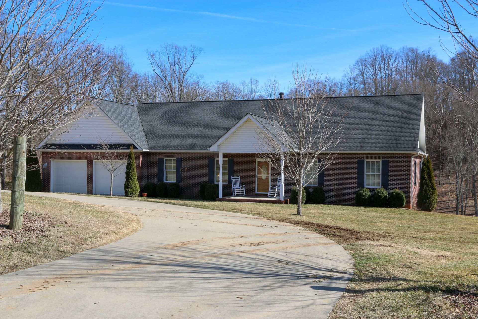 Single-story brick house with two garages, curved driveway, and leafless trees under a blue sky