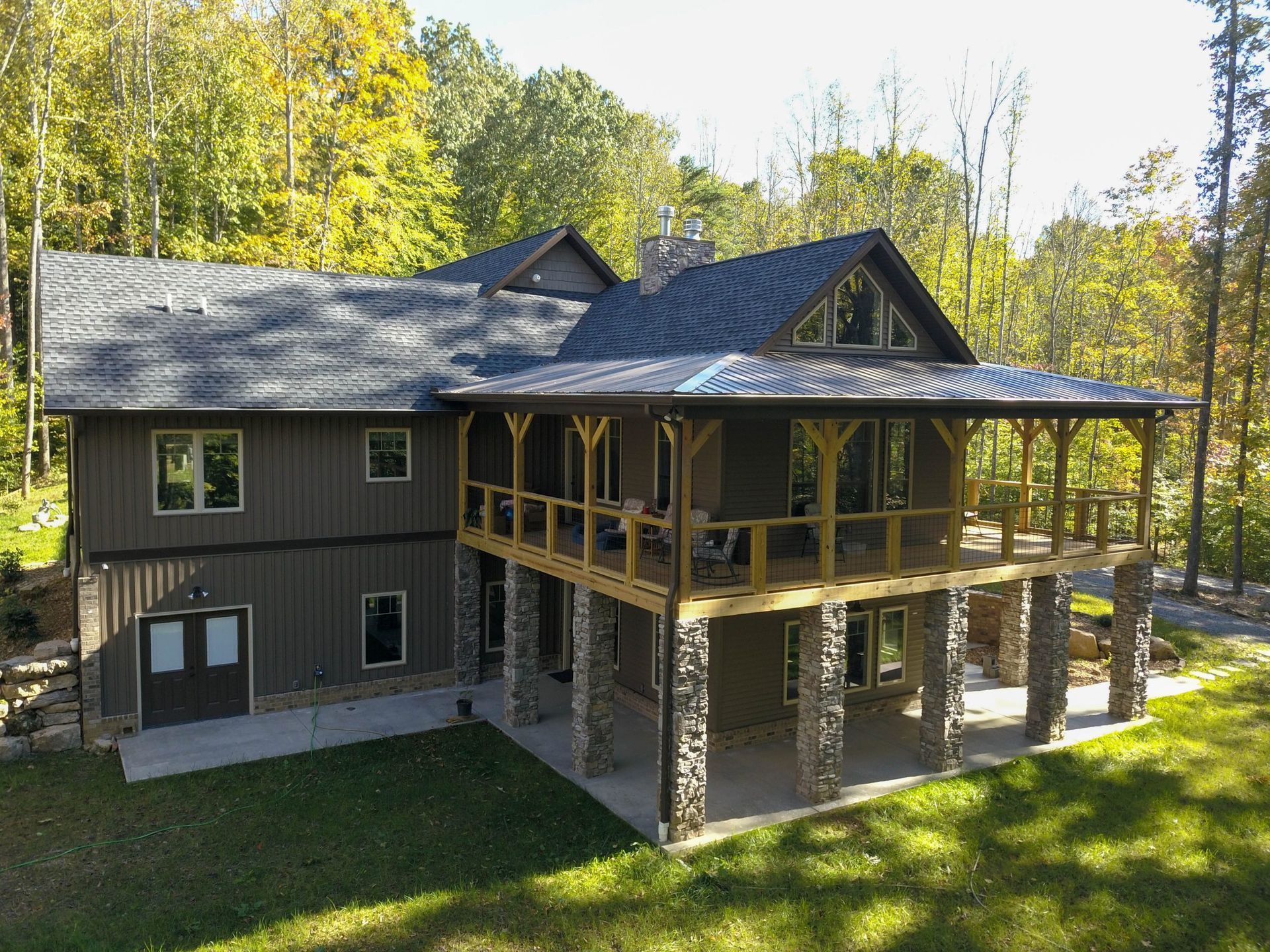 Two-story house with stone pillars and a covered porch, surrounded by trees and lawn