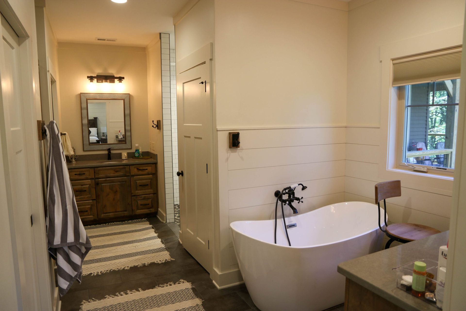 Bathroom interior with freestanding tub, vanity, mirror, striped rug, and window light