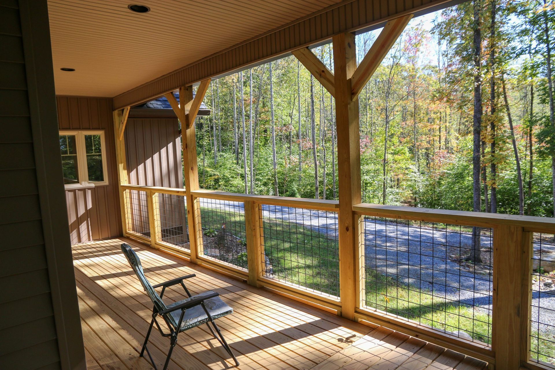 Covered wooden porch with rocking chair overlooking a wooded yard and road