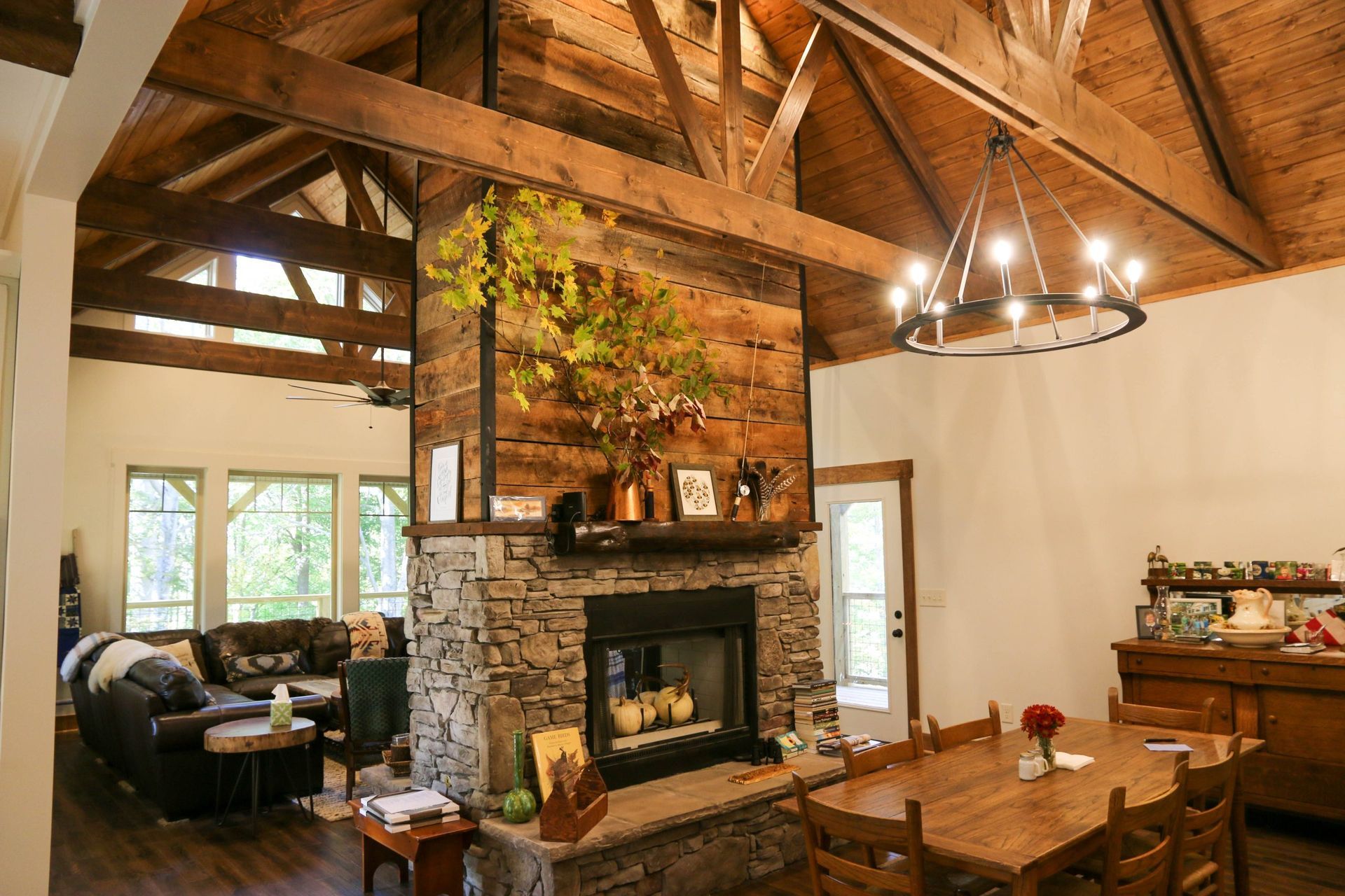 Rustic living room with wood beams, stone fireplace, chandelier, and dining table