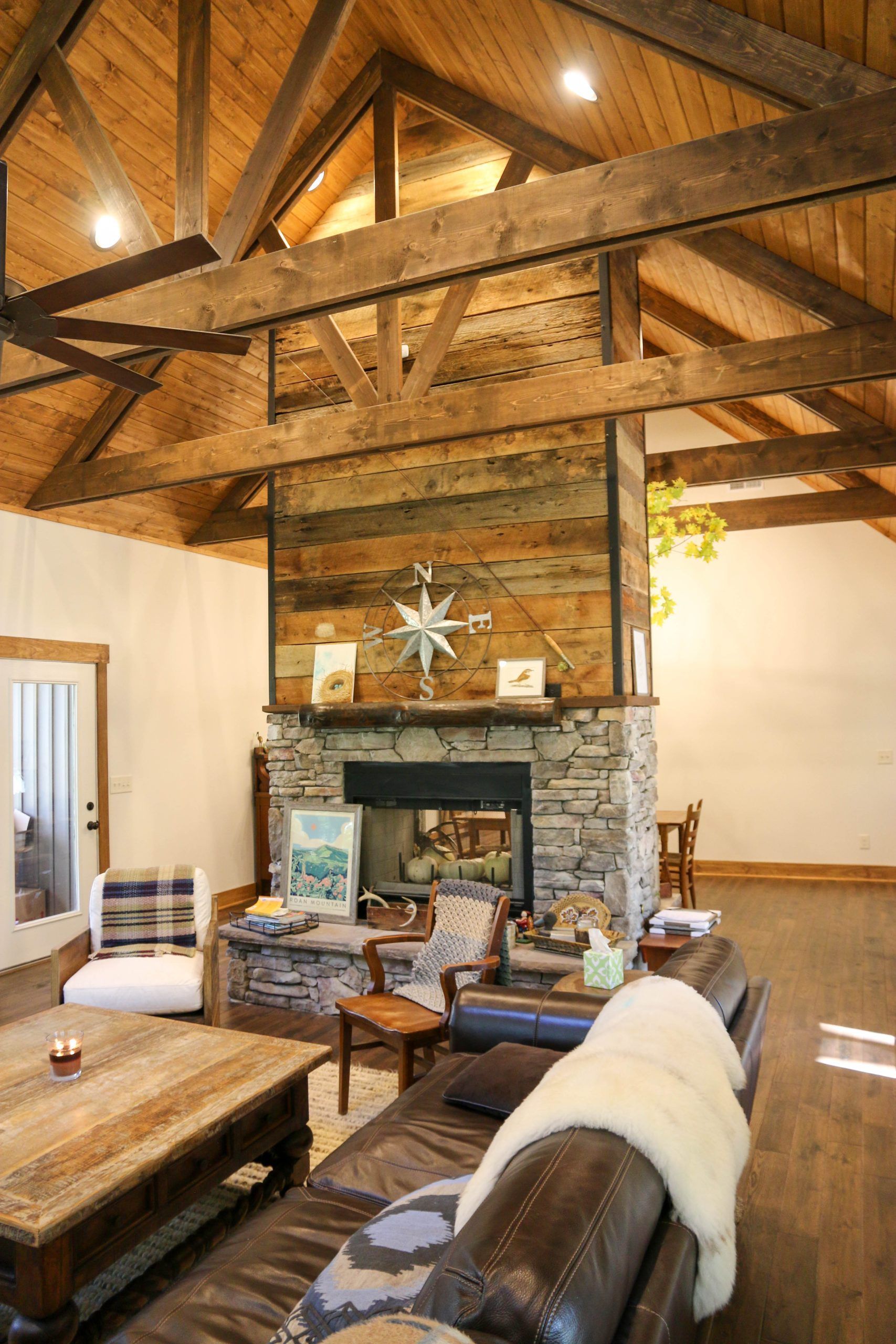 Rustic living room with stone fireplace, exposed wood beams, and leather sofas under warm lighting