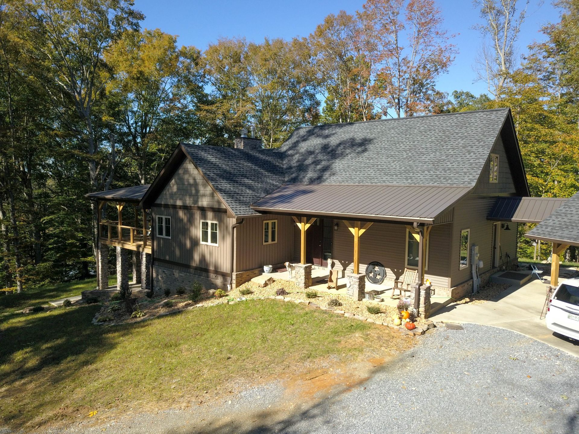 Brown house with dark roof and front porch on a wooded hillside under a clear blue sky