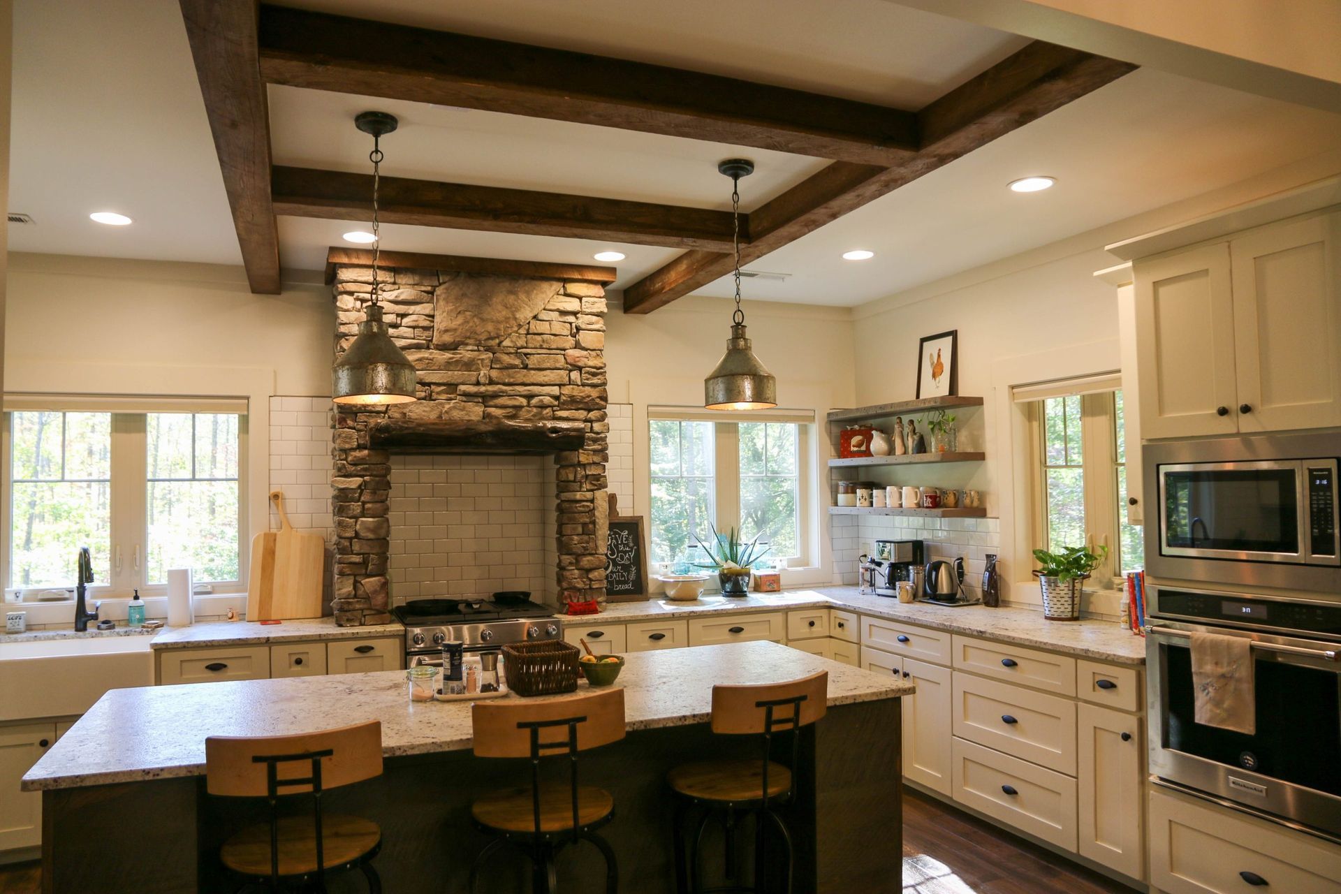 Bright kitchen with stone fireplace, large island, pendant lights, and cream cabinets