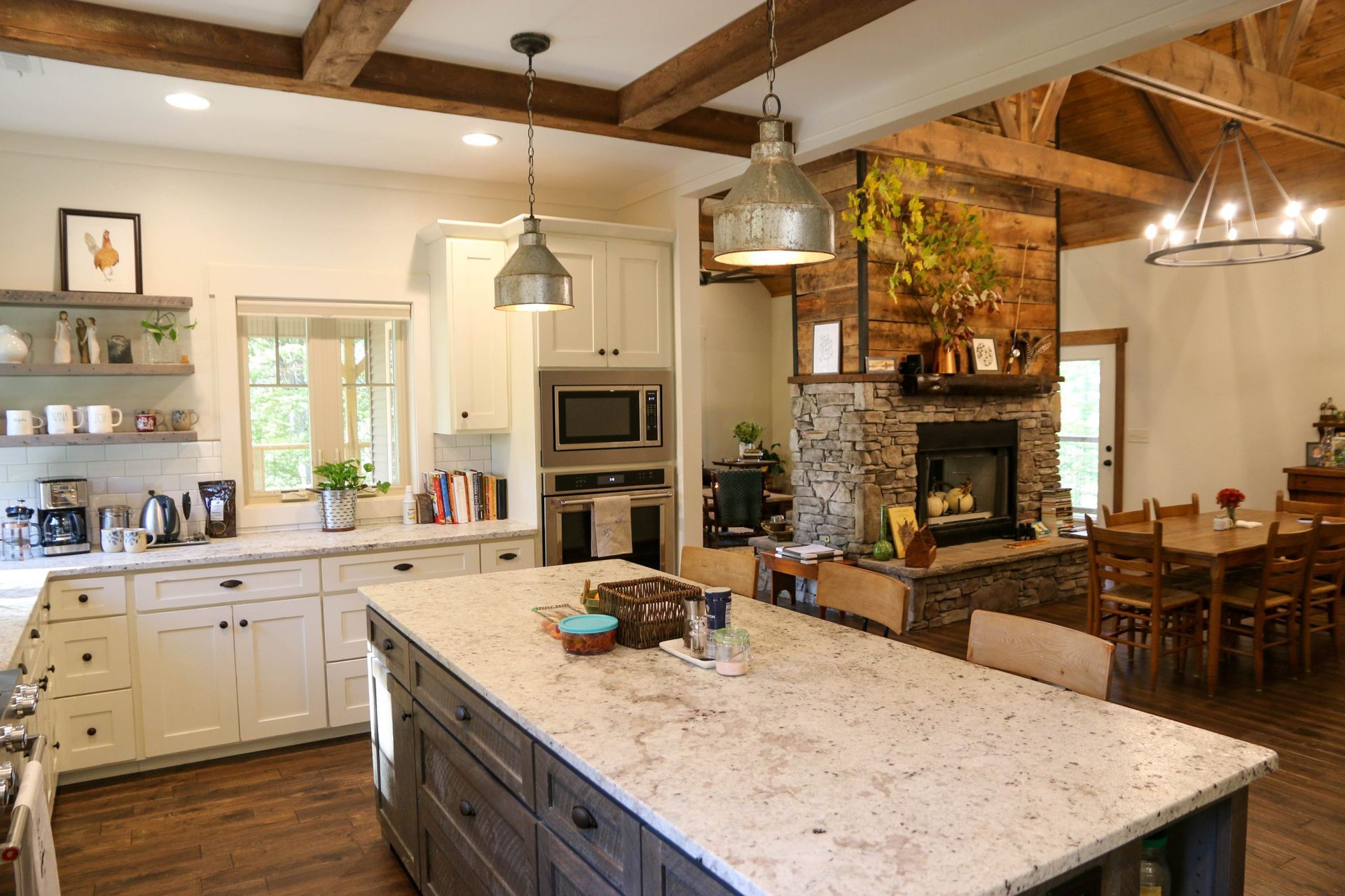 Bright kitchen with large island, white cabinets, pendant lights, and rustic beams opening to a dining area