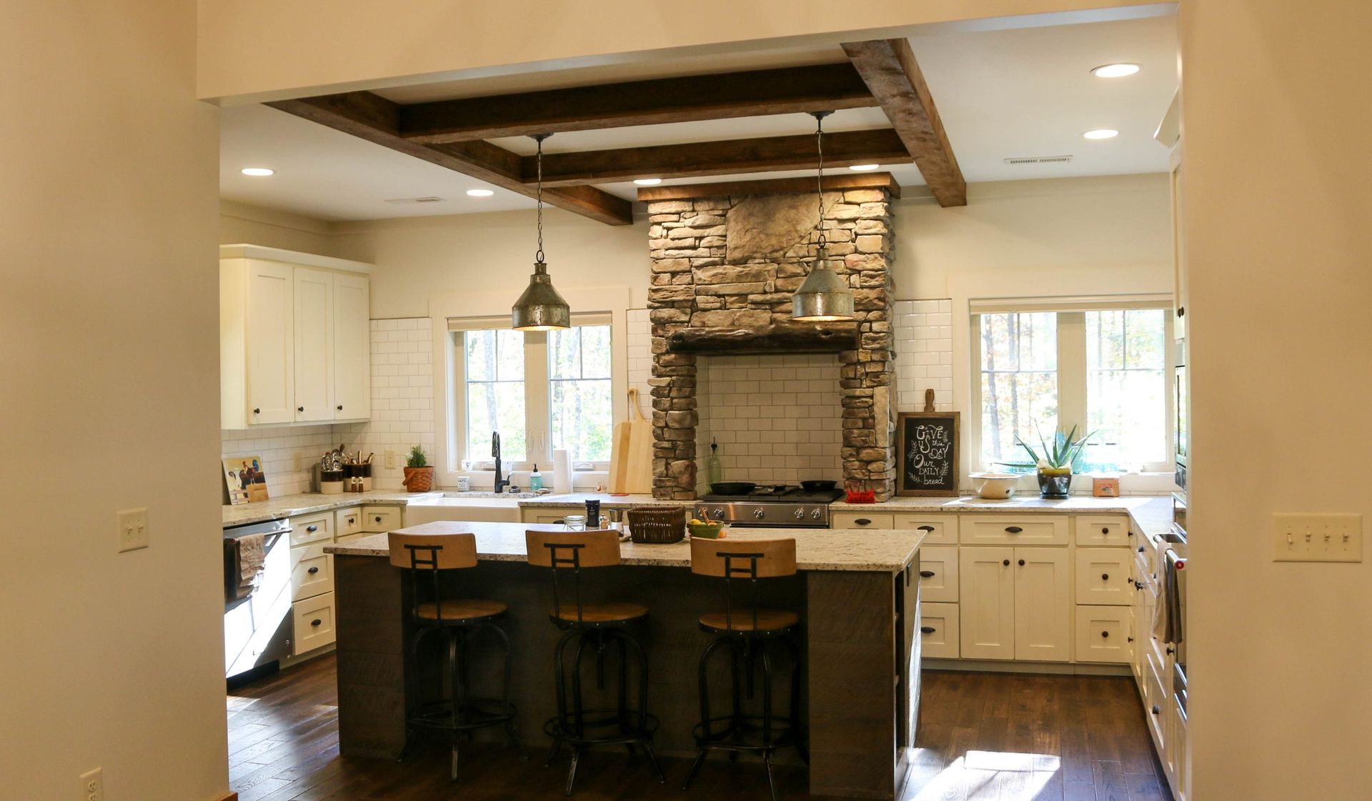 Open kitchen with stone fireplace, white cabinets, dark island, and wood floors in a bright home interior