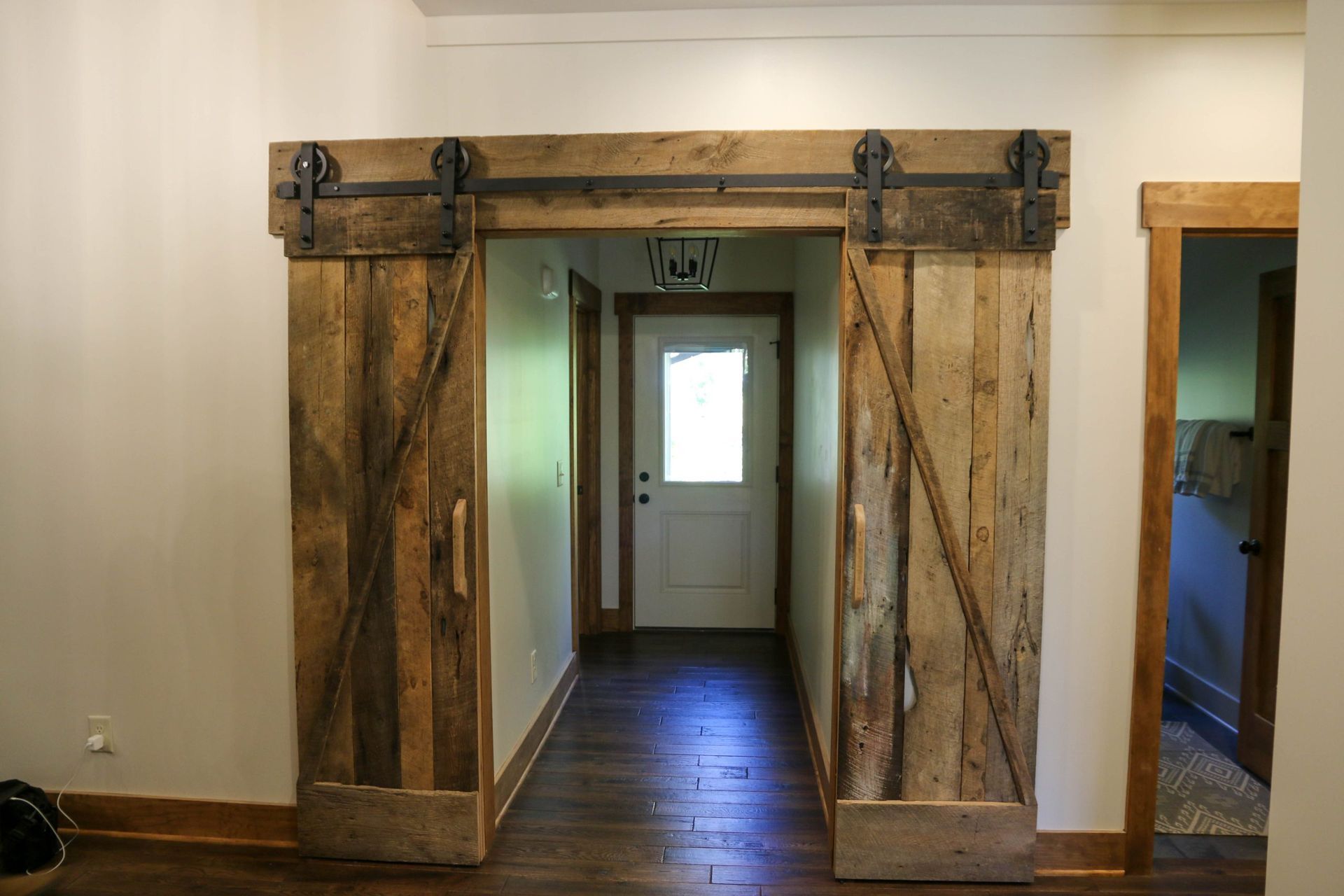 Rustic wooden barn doors frame a hallway with a white door at the far end.