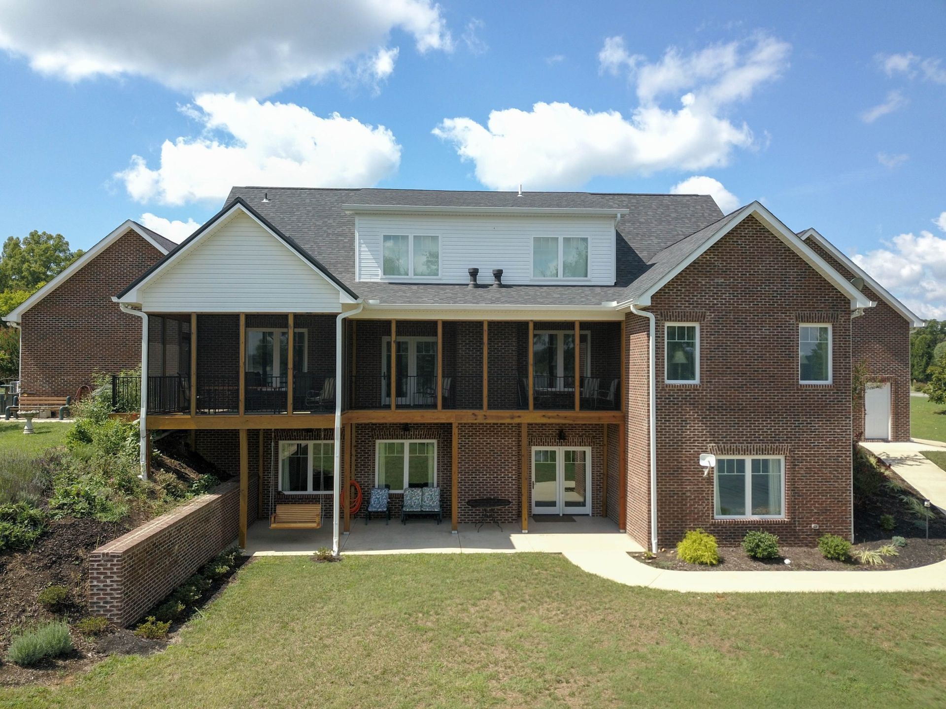 Two-story brick house with a screened porch, white-trimmed upper windows, and a green lawn under a blue sky.