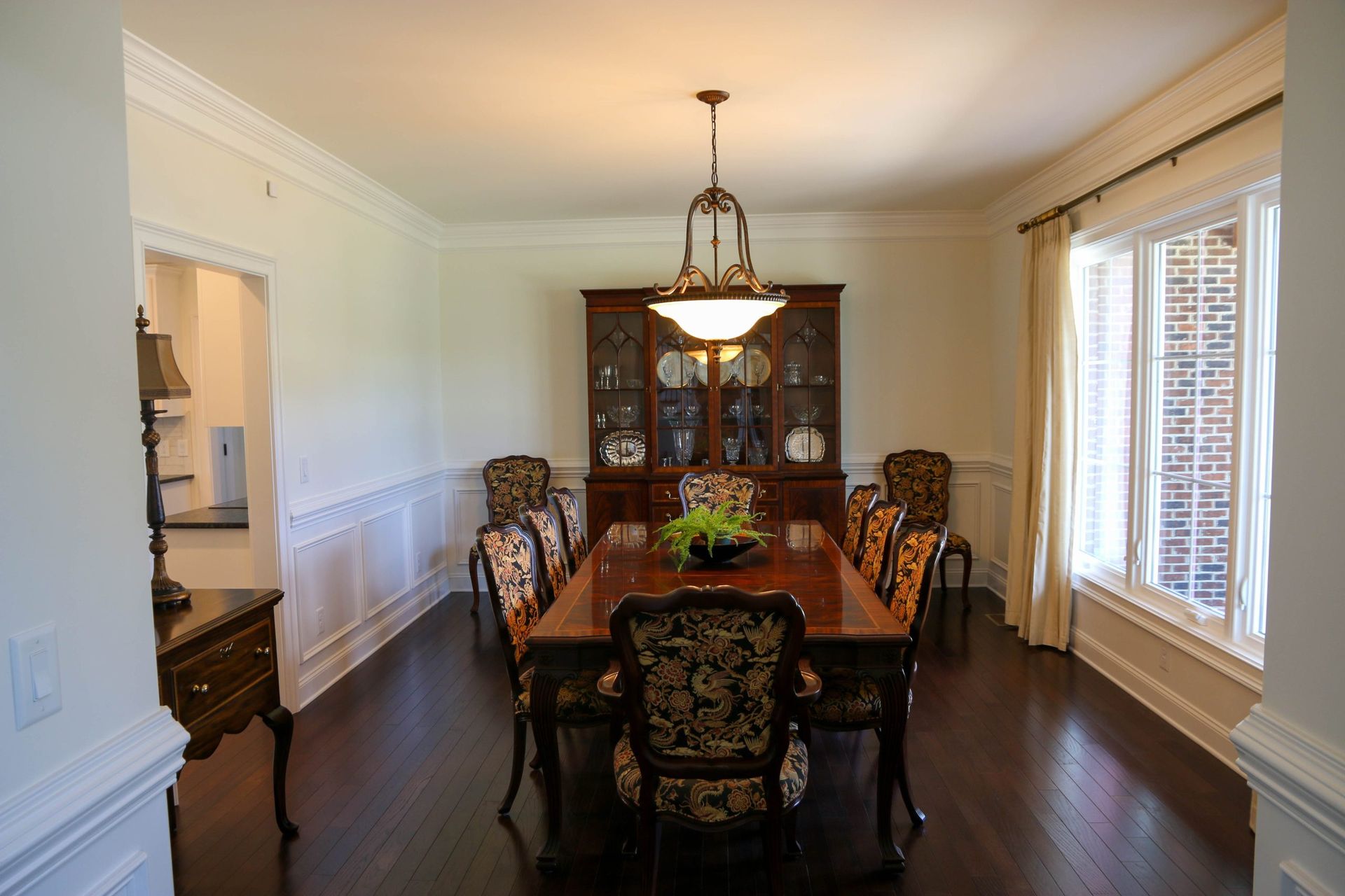 Formal dining room with dark wood table, ornate chairs, chandelier, and large windows with blinds