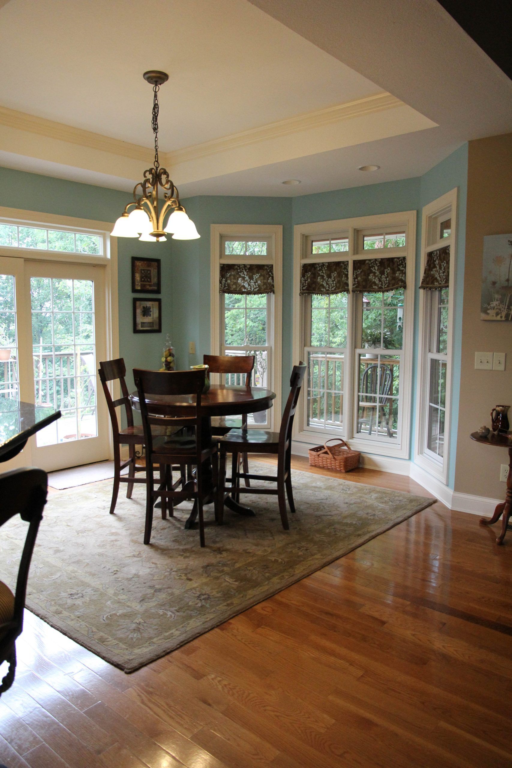 Dining room with round table, chairs, chandelier, large windows, hardwood floors, and a patterned rug.