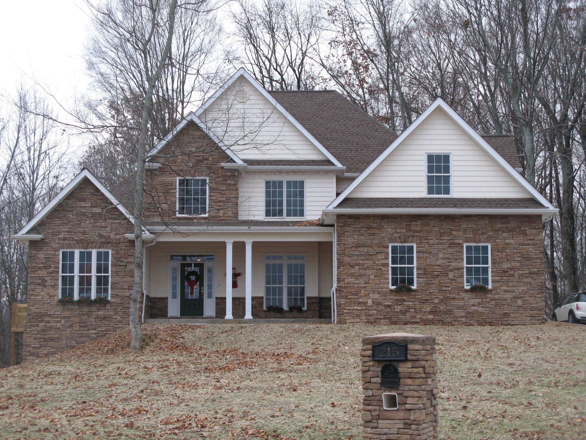 Suburban brick and beige two-story house with a front porch and a mailbox in the yard.