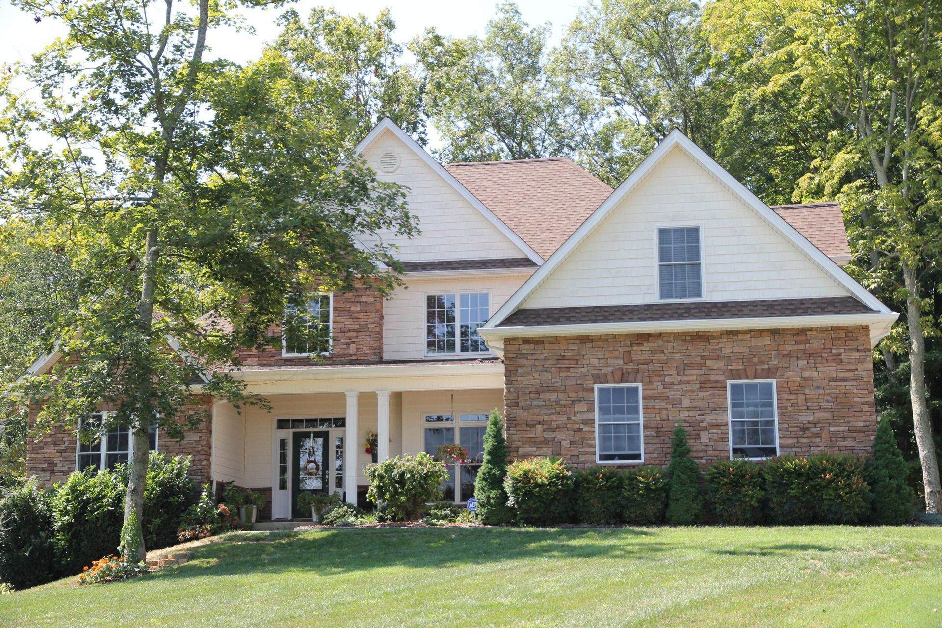 Two-story brick-and-white house with a front porch, surrounded by trees and a green lawn
