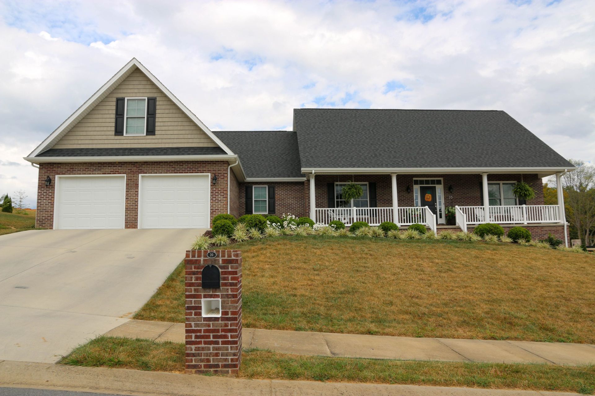 Suburban house with two-car garage, front porch, and brick mailbox by the driveway.