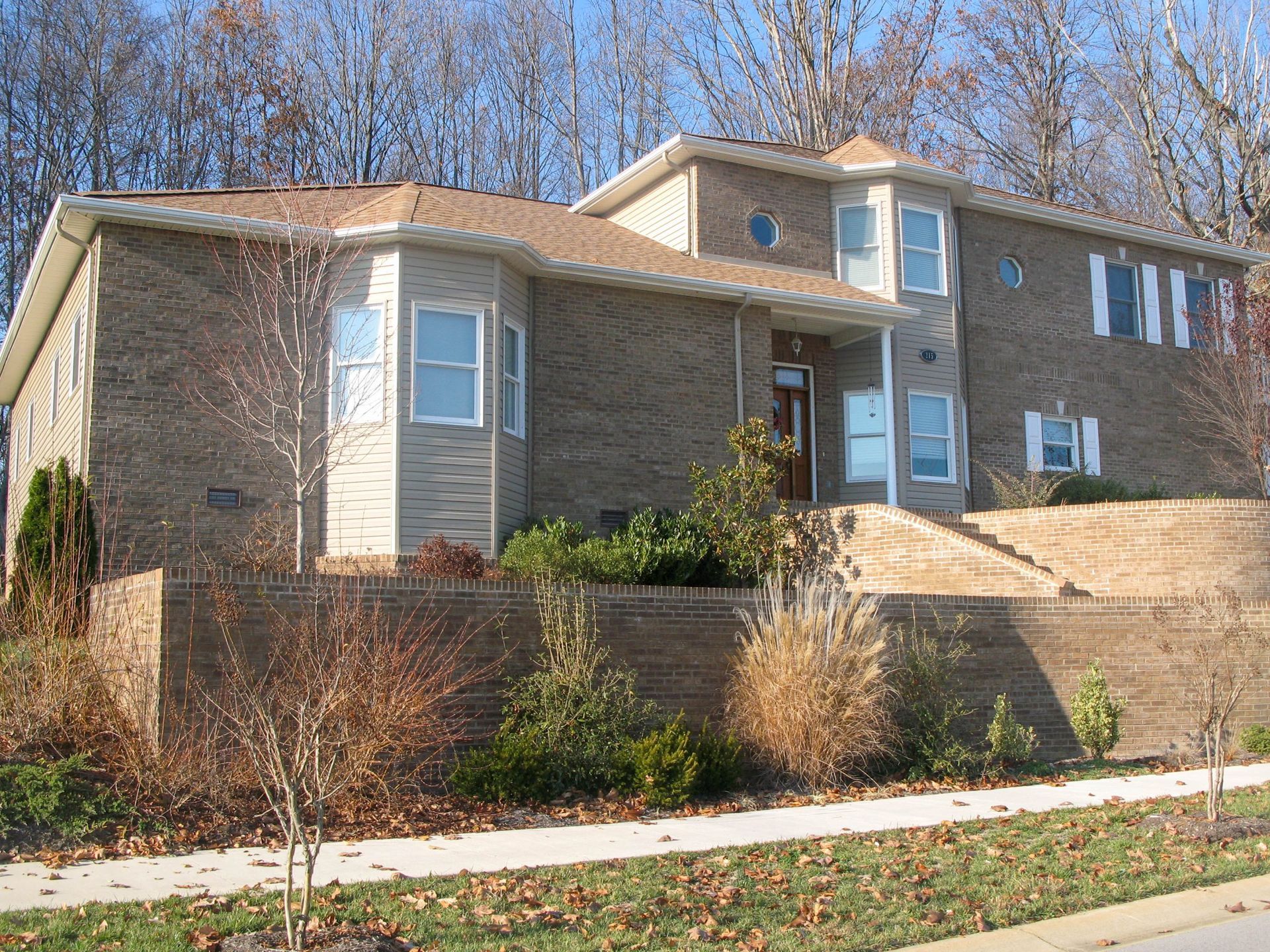 Suburban brick house with beige siding and a landscaped front yard under a clear blue sky
