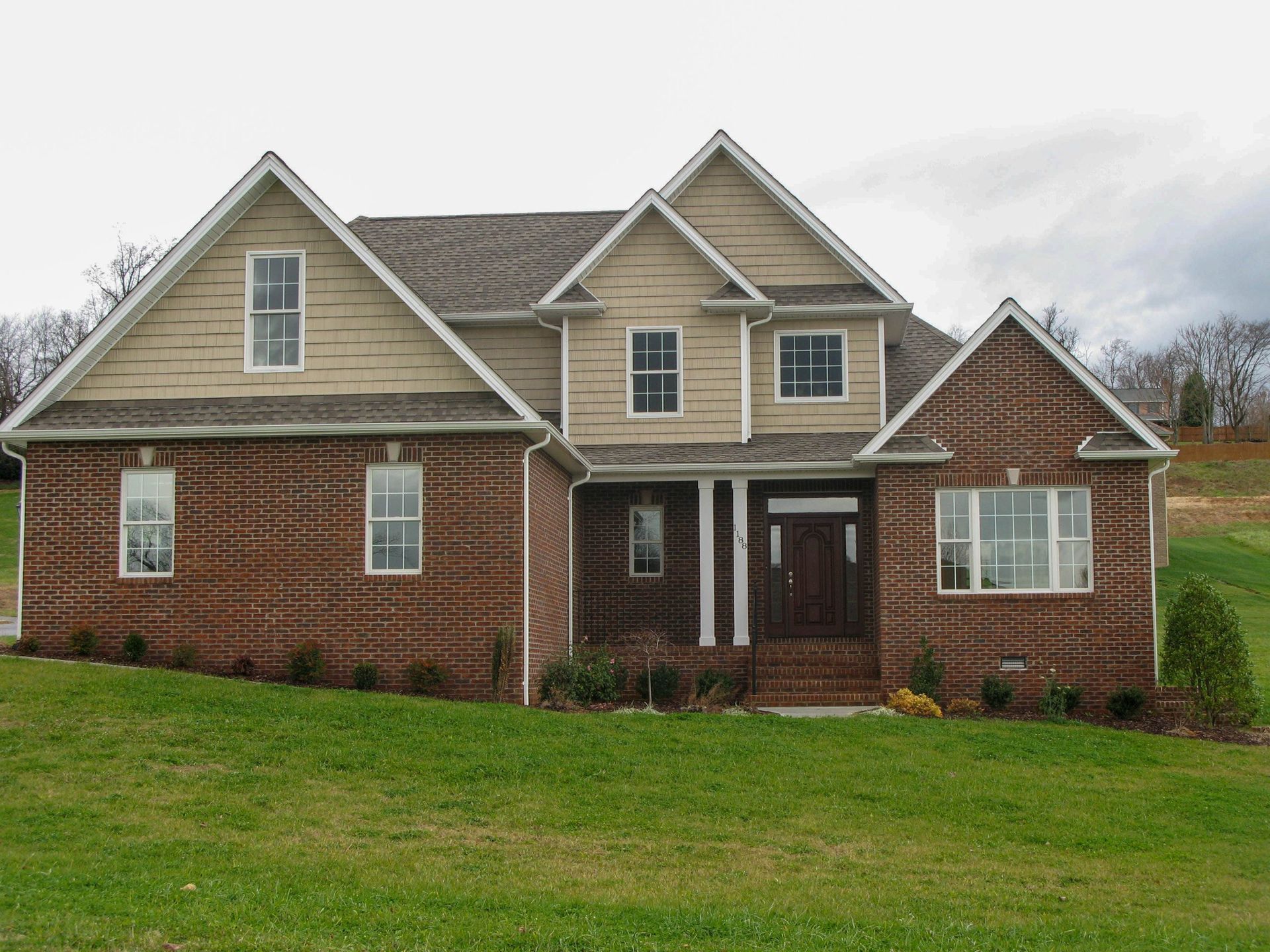 Brick and tan suburban house with a gabled roof and front porch on a grassy lawn