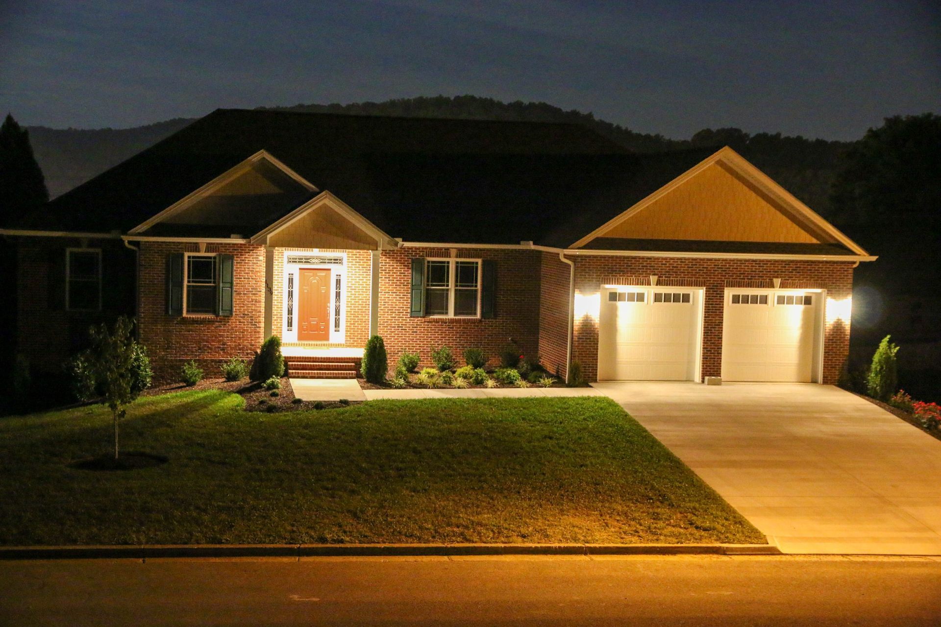 Lit suburban house with front porch and two-car garage at night