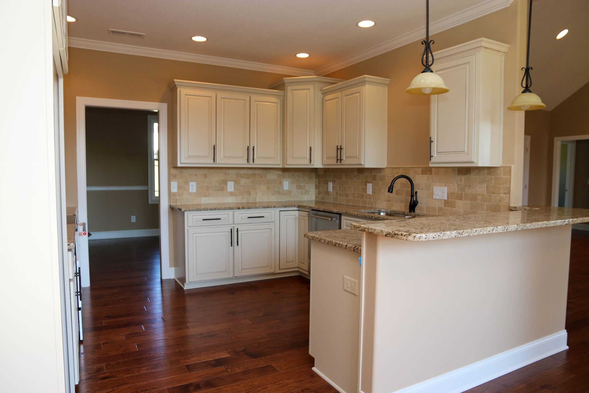 Bright kitchen with white cabinets, granite island, hardwood floors, and pendant lights