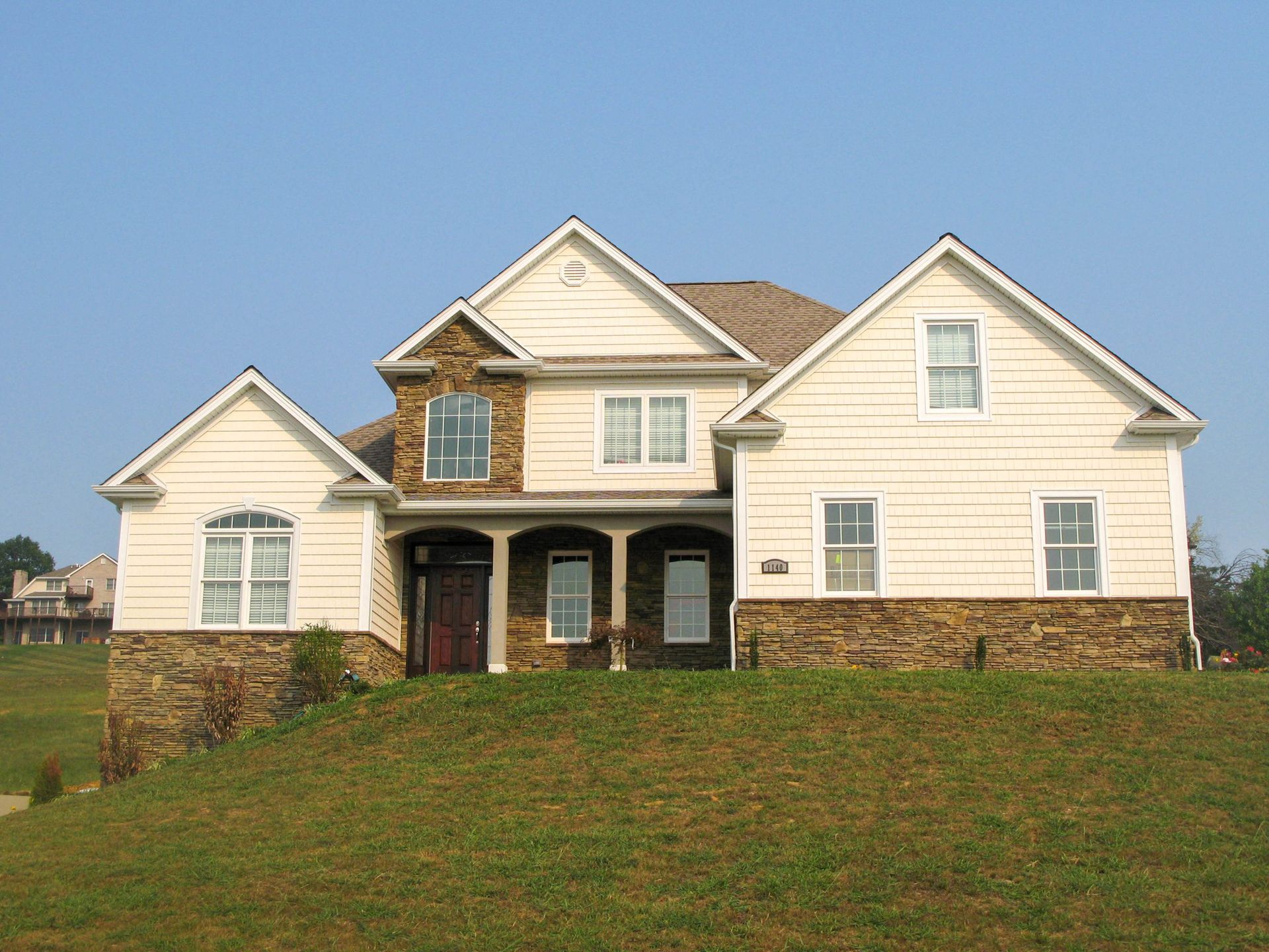 Large cream-colored suburban house with stone accents and a grassy front lawn under a clear sky