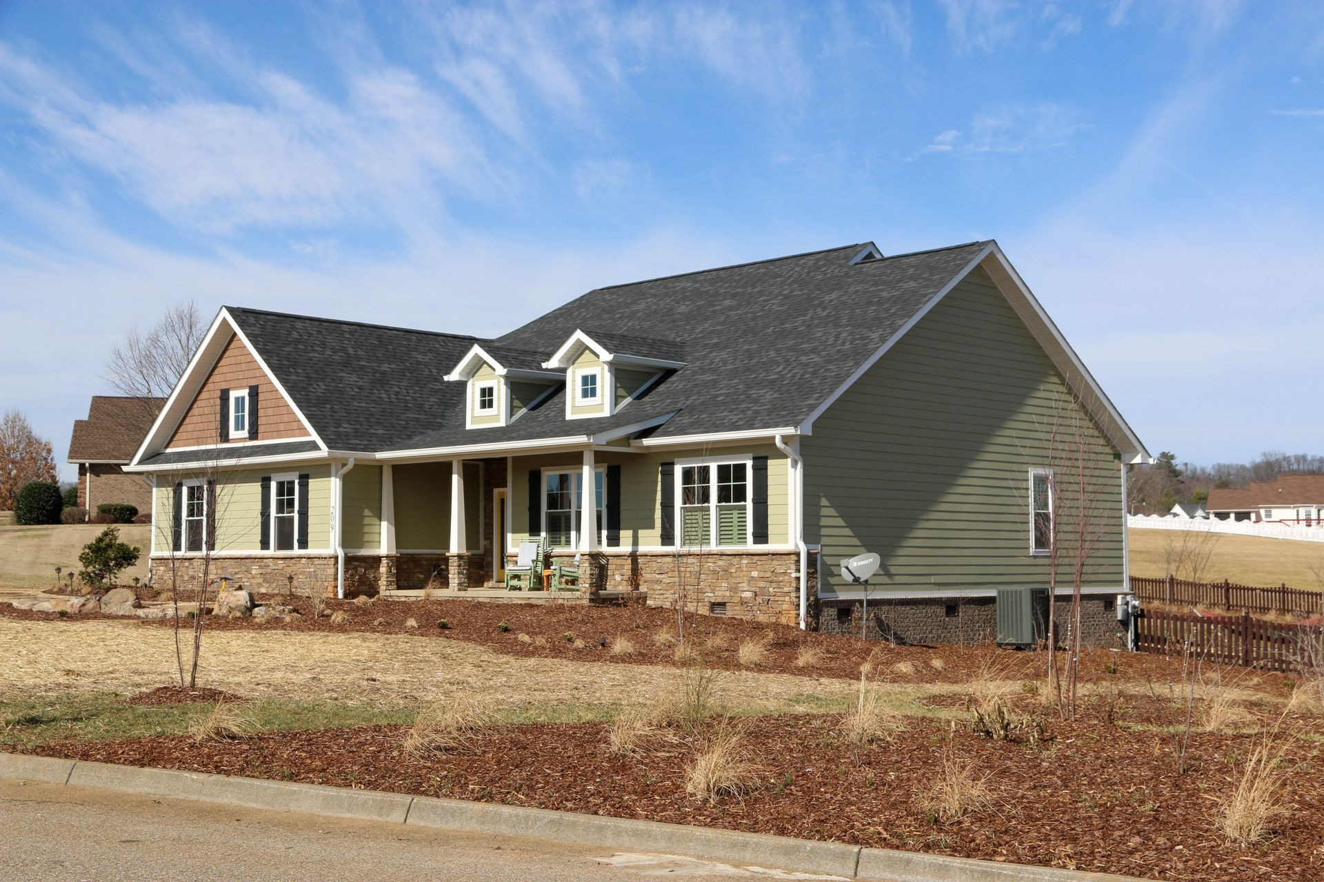 Suburban house with gray siding, brick accents, and a front porch under a blue sky