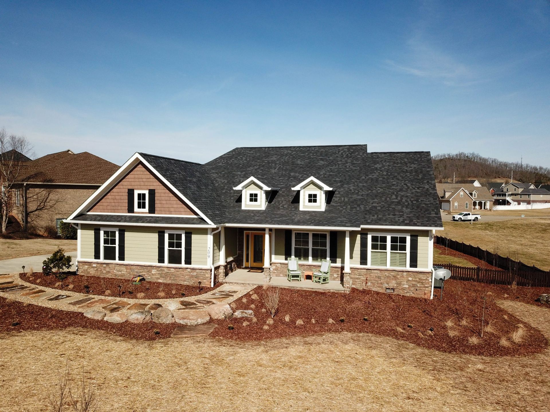 Large two-story house with gray roof, beige siding, stone porch, and red mulch in a suburban lot